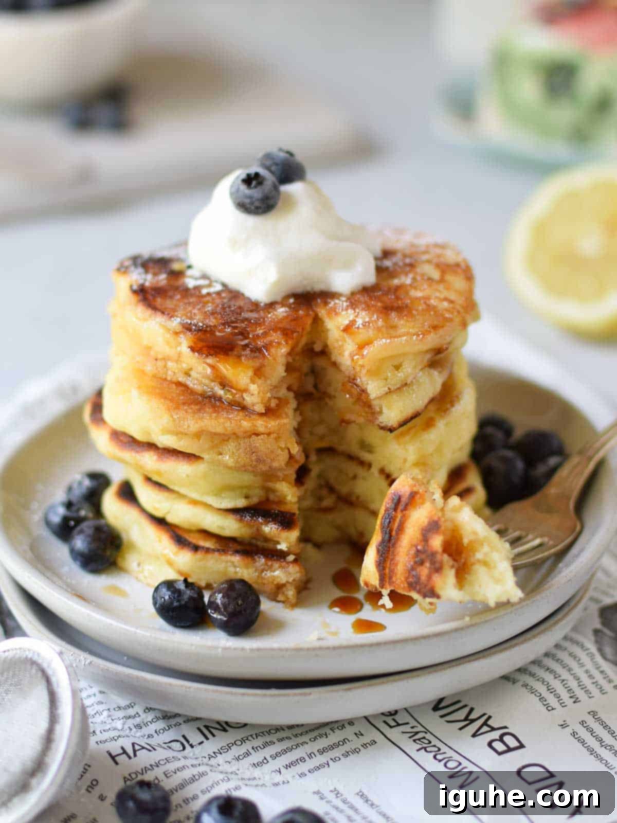 Dreamy Lemon Mascarpone Pancakes 8 Lemon mascarpone pancakes stacked with blueberries, one with a bite taken out, showing the fluffy interior.
