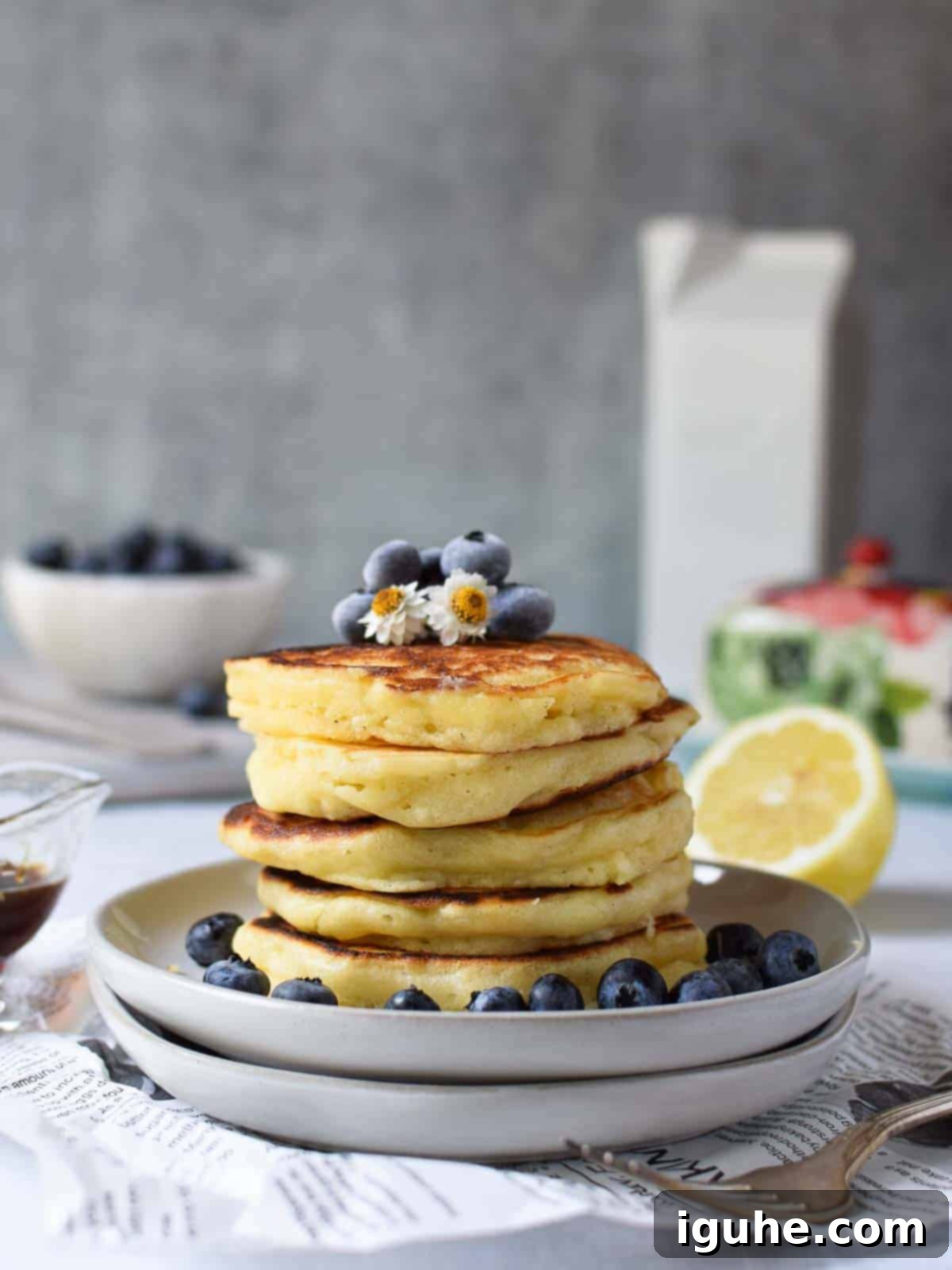 Dreamy Lemon Mascarpone Pancakes 9 Lemon pancakes stacked on plates with blueberries on top, ready for serving with syrup.