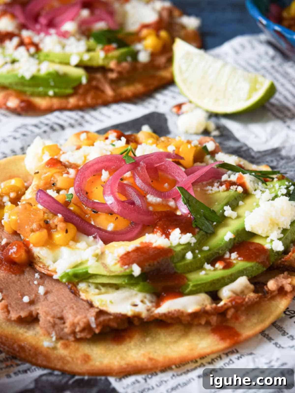 Huevos rancheros tostadas on newspaper with a lime in the background.