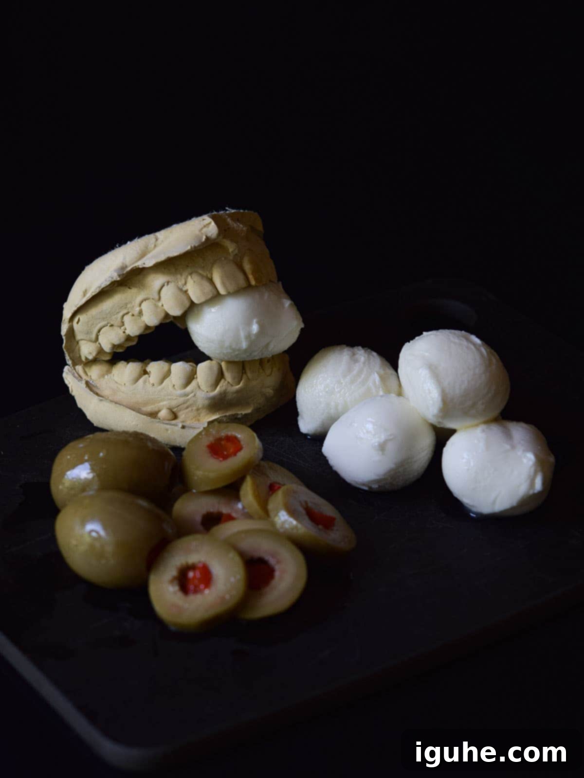 Halloween's Bloody Scary Mary 3 Fresh mozzarella pearls and pitted green olives on a black surface, ready for making spooky eyeball garnishes.