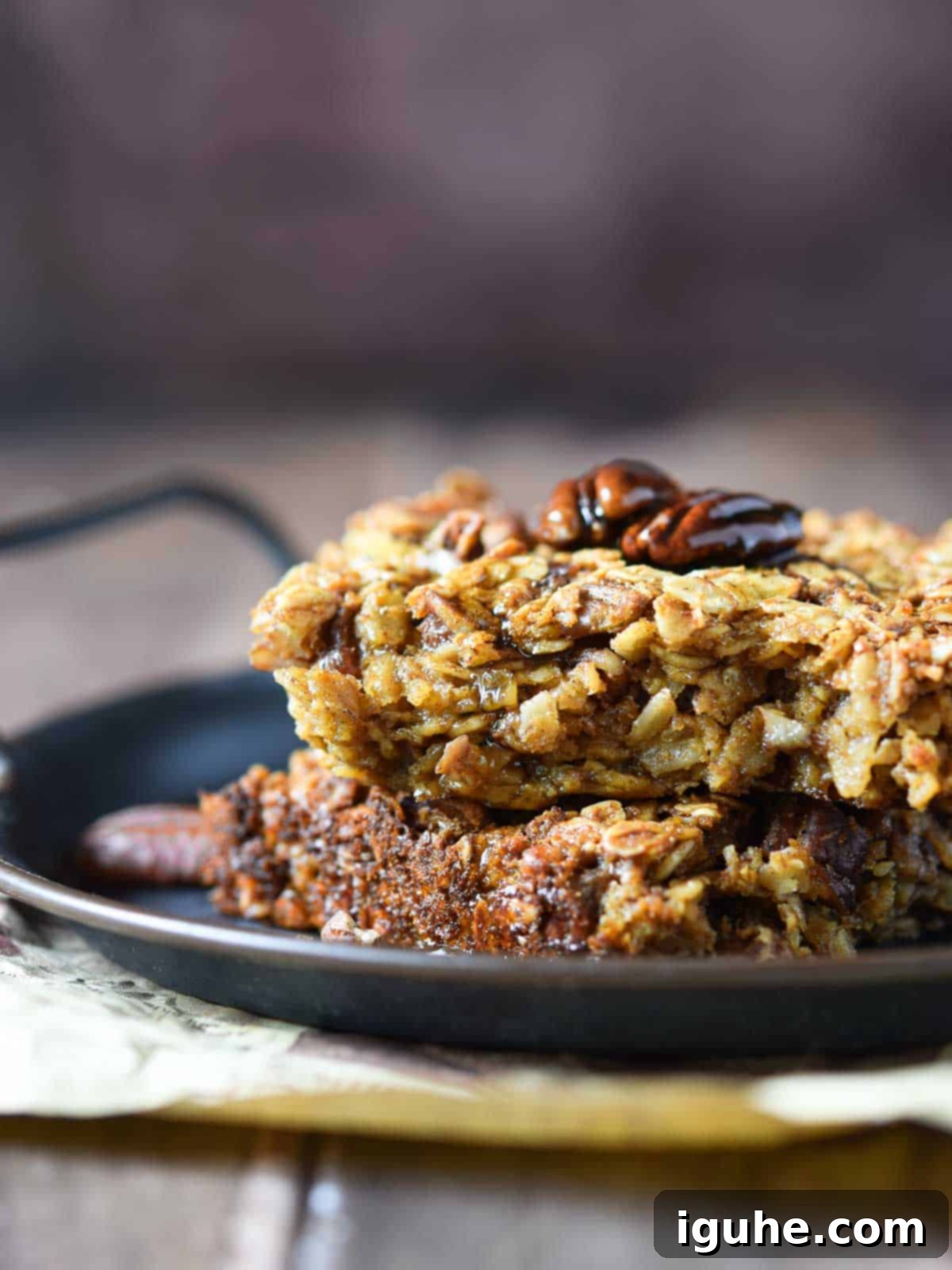 Decadent Pecan Pie Baked Oatmeal 8 Pecan pie baked oatmeal squares stacked on a black tray with a warm brown background.
