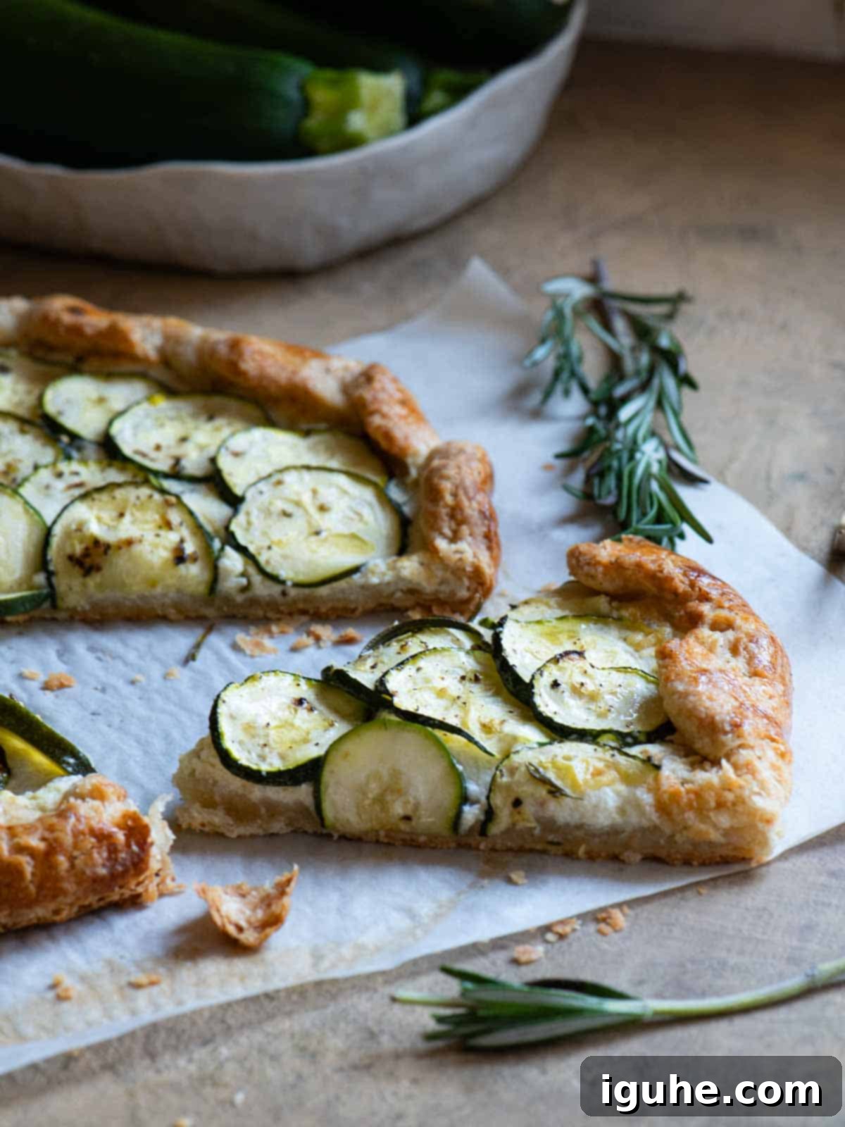 Rustic Zucchini Ricotta Tart 6 A slice of zucchini galette cut out on parchment paper with rosemary in the background.