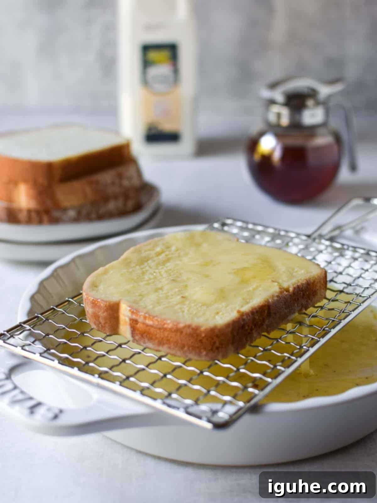 Repurposed Buttermilk French Toast 7 A soaked bread slice for French toast being held over a white bowl to drain excess custard.