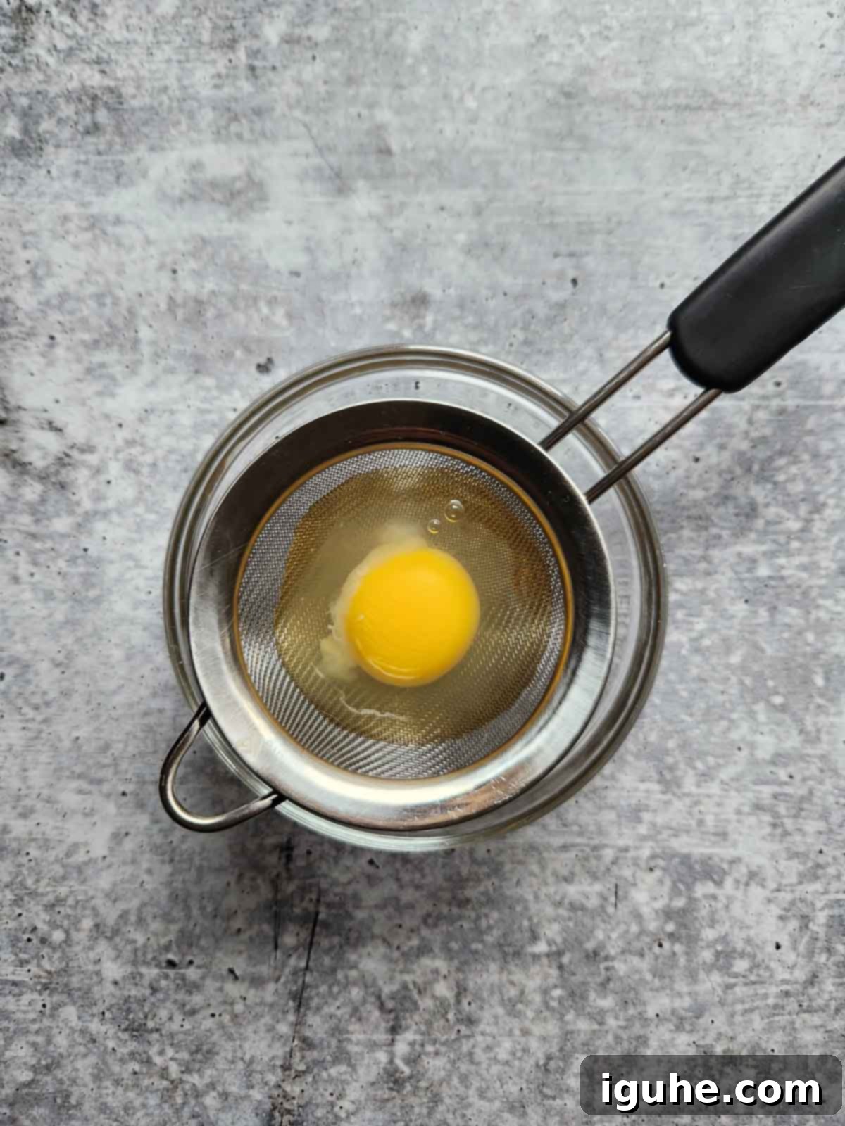 Fiesta Benedict with Chipotle Kick 5 An egg being strained over a clear bowl to remove excess whites before poaching.