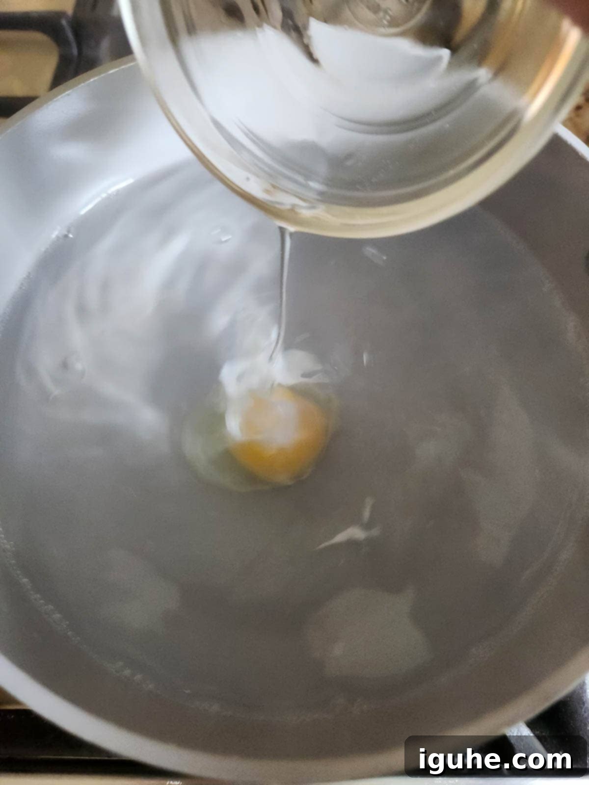 Fiesta Benedict with Chipotle Kick 7 A prepared egg being carefully dropped into the center of a swirling pot of simmering water for poaching.