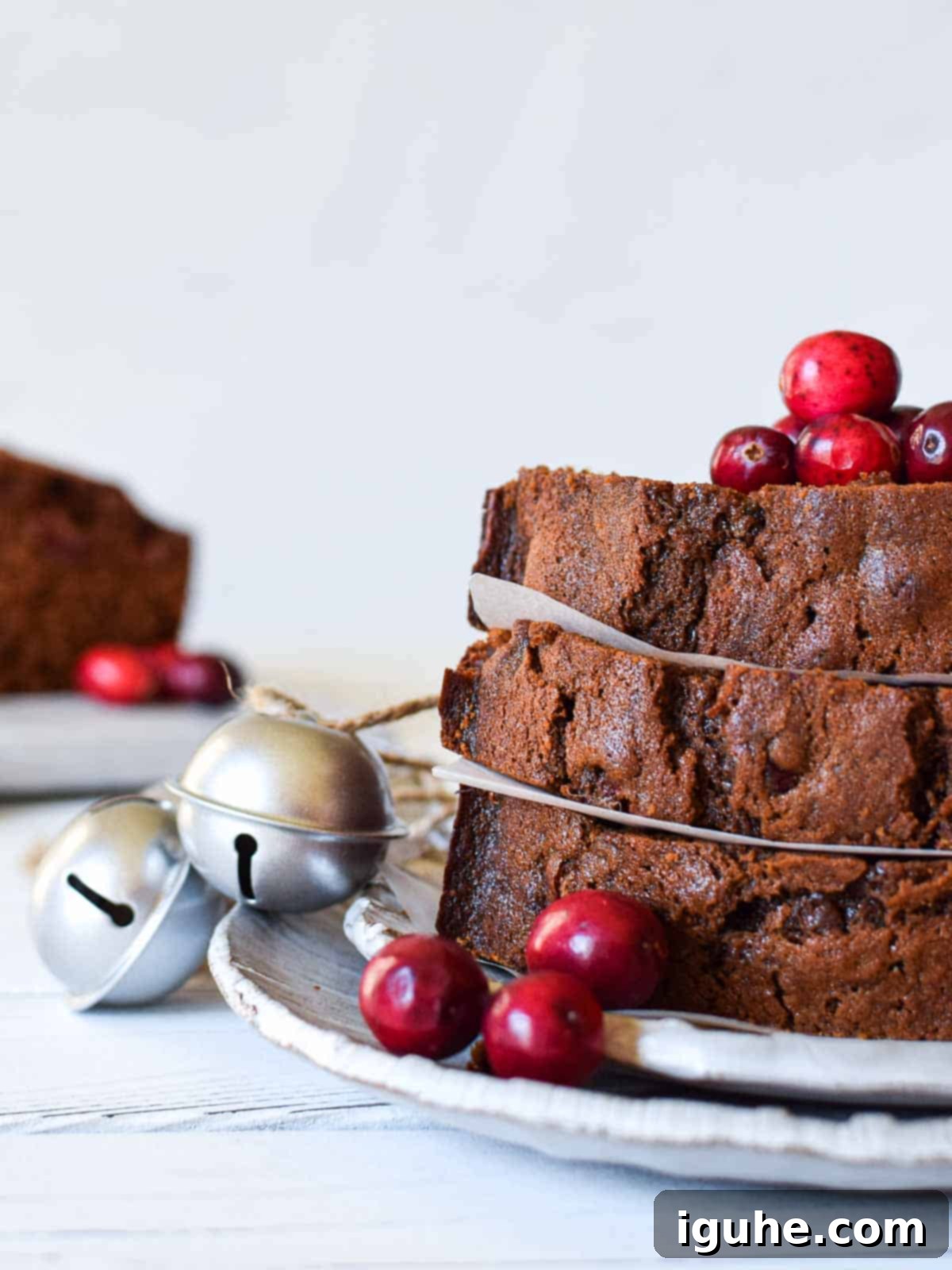 Gingerbread Cranberry Loaf 3 Eye-level view of slices of cranberry loaf arranged beautifully with festive cranberries and small bells next to it, highlighting the holiday theme.