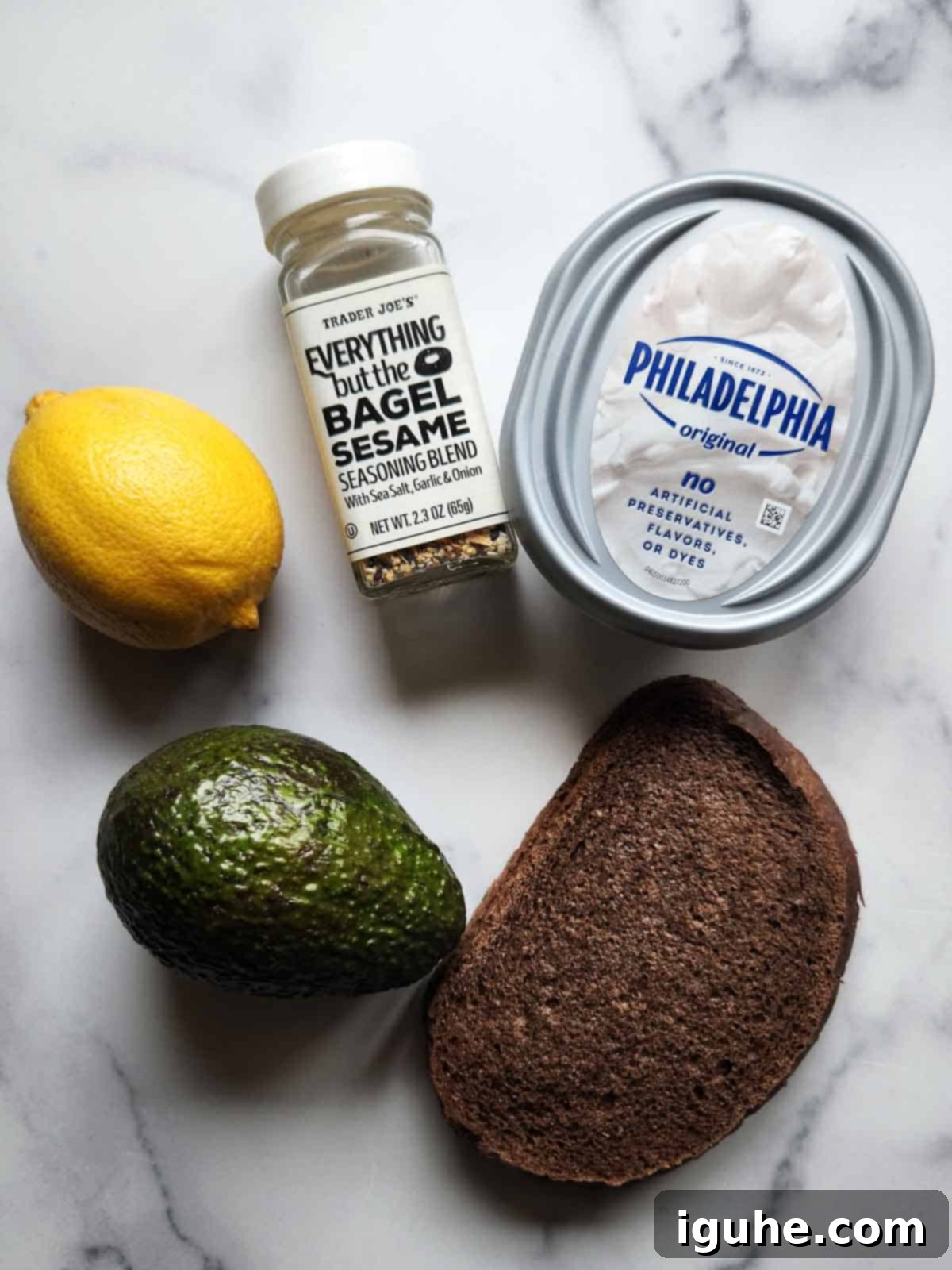 Gourmet Cream Cheese Avocado Toast 3 A selection of fresh ingredients for avocado cream cheese toast: pumpernickel bread, a block of cream cheese, a ripe avocado, everything bagel seasoning, and fresh lemons.