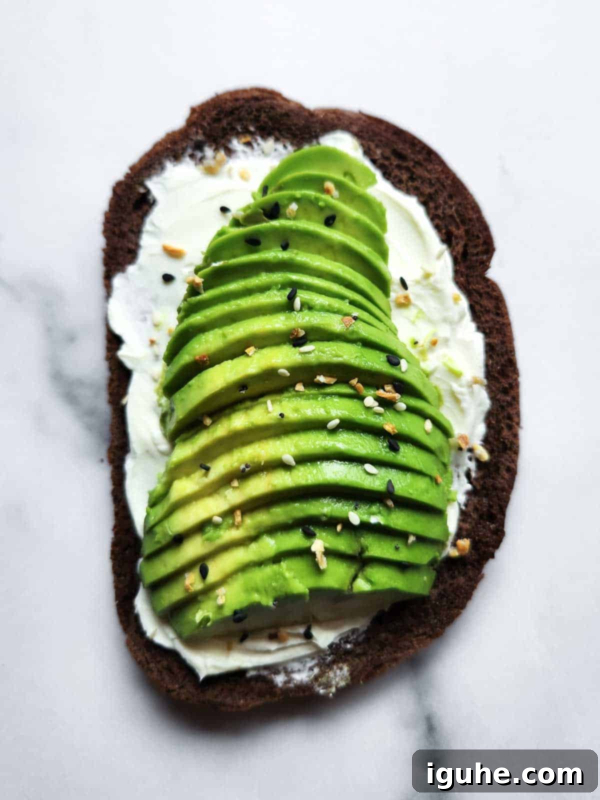 Gourmet Cream Cheese Avocado Toast 7 Cream cheese and avocado toast finished with a generous sprinkle of everything bagel seasoning and a drizzle of lemon juice, presented on a white background.