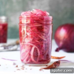 Sweet Heat Pickled Onions 10 Pickled red onions in a clear mason jar on a white board, highlighting their vibrant color and texture.