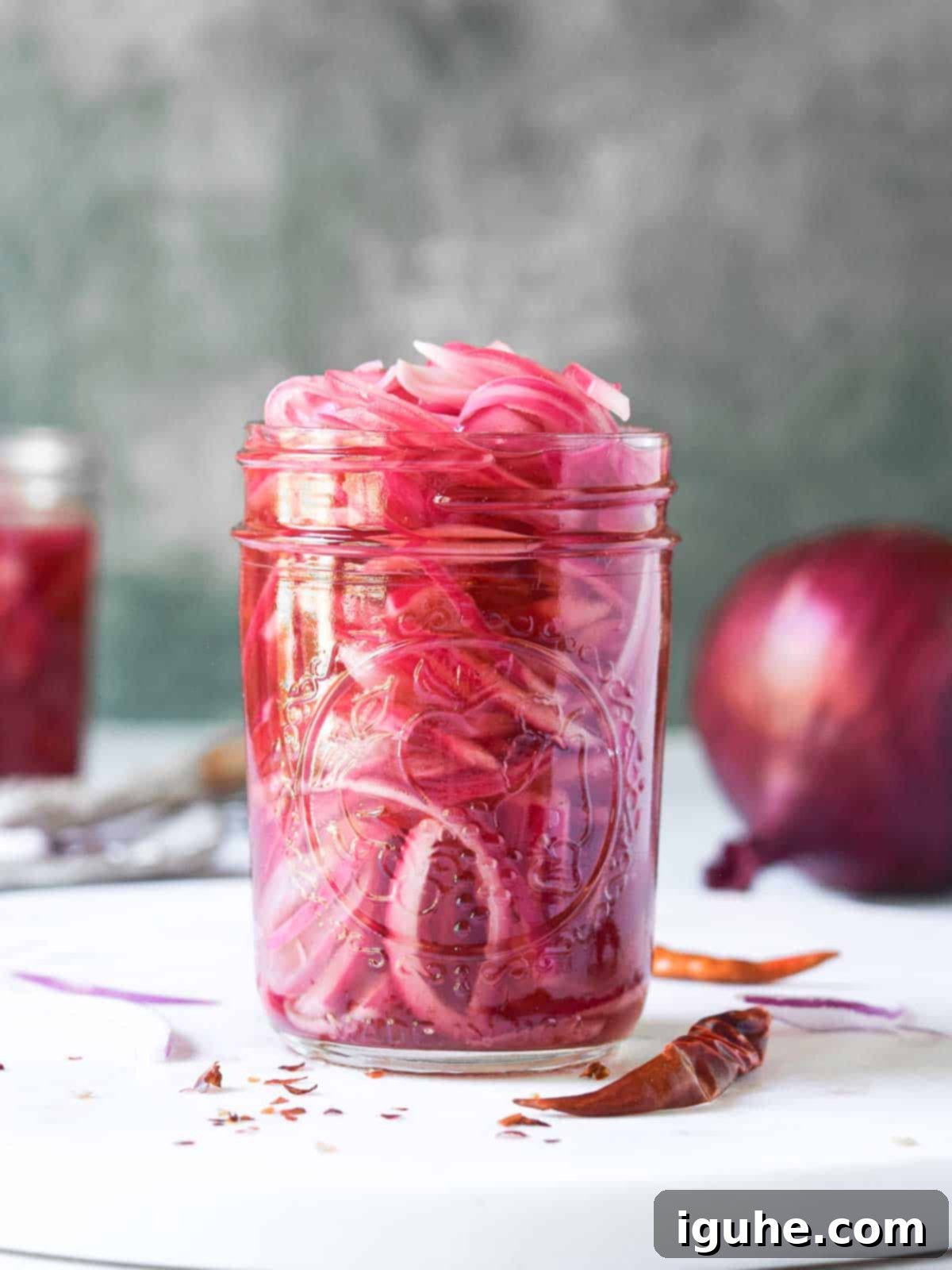 Sweet Heat Pickled Onions 3 Pickled red onions in a clear mason jar on a white surface, showcasing their vibrant pink color.