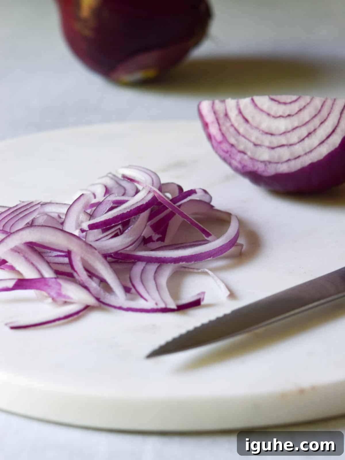 Sweet Heat Pickled Onions 4 Thinly sliced red onions on a white marble cutting board, ready for pickling.
