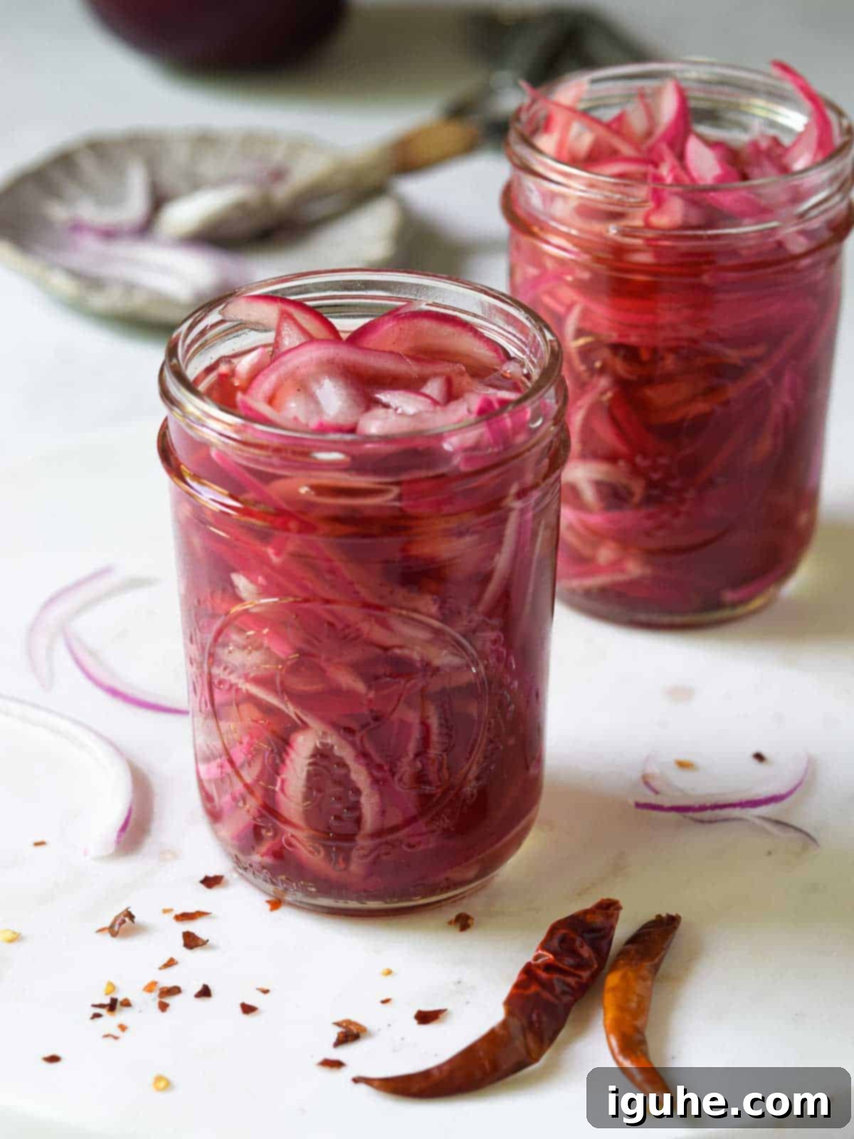 Sweet Heat Pickled Onions 9 Pickled red onions in a clear Mason jar on a white marble surface, highlighting their beautiful pink color.