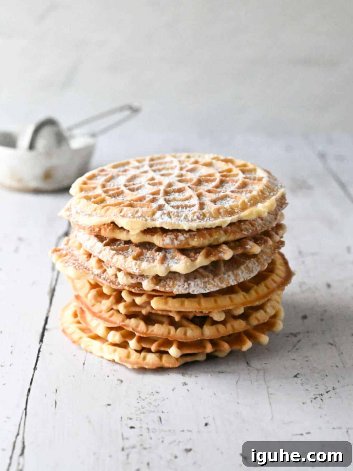 Stacked lemon pizzelle cookies dusted with powdered sugar, with a fresh lemon in the background.
