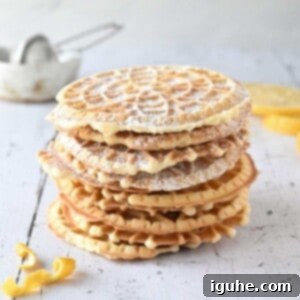 Effortless Lemon Pizzelle 14 Lemon pizzelles stacked on top of each other on white wood with lemon in the background.