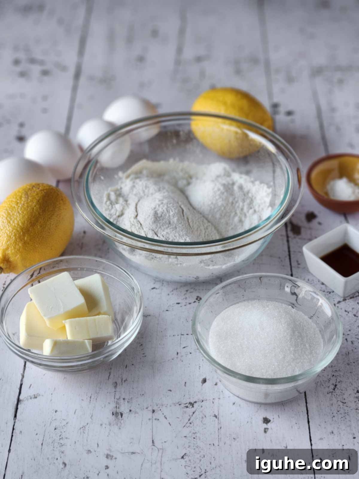 Effortless Lemon Pizzelle 3 Ingredients for lemon pizzelles on white wood, including flour, sugar, eggs, butter, vanilla, and lemons.