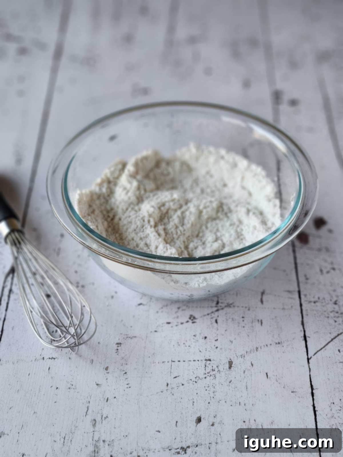 Effortless Lemon Pizzelle 4 Flour and baking powder sifted in a clear bowl with a whisk next to it.