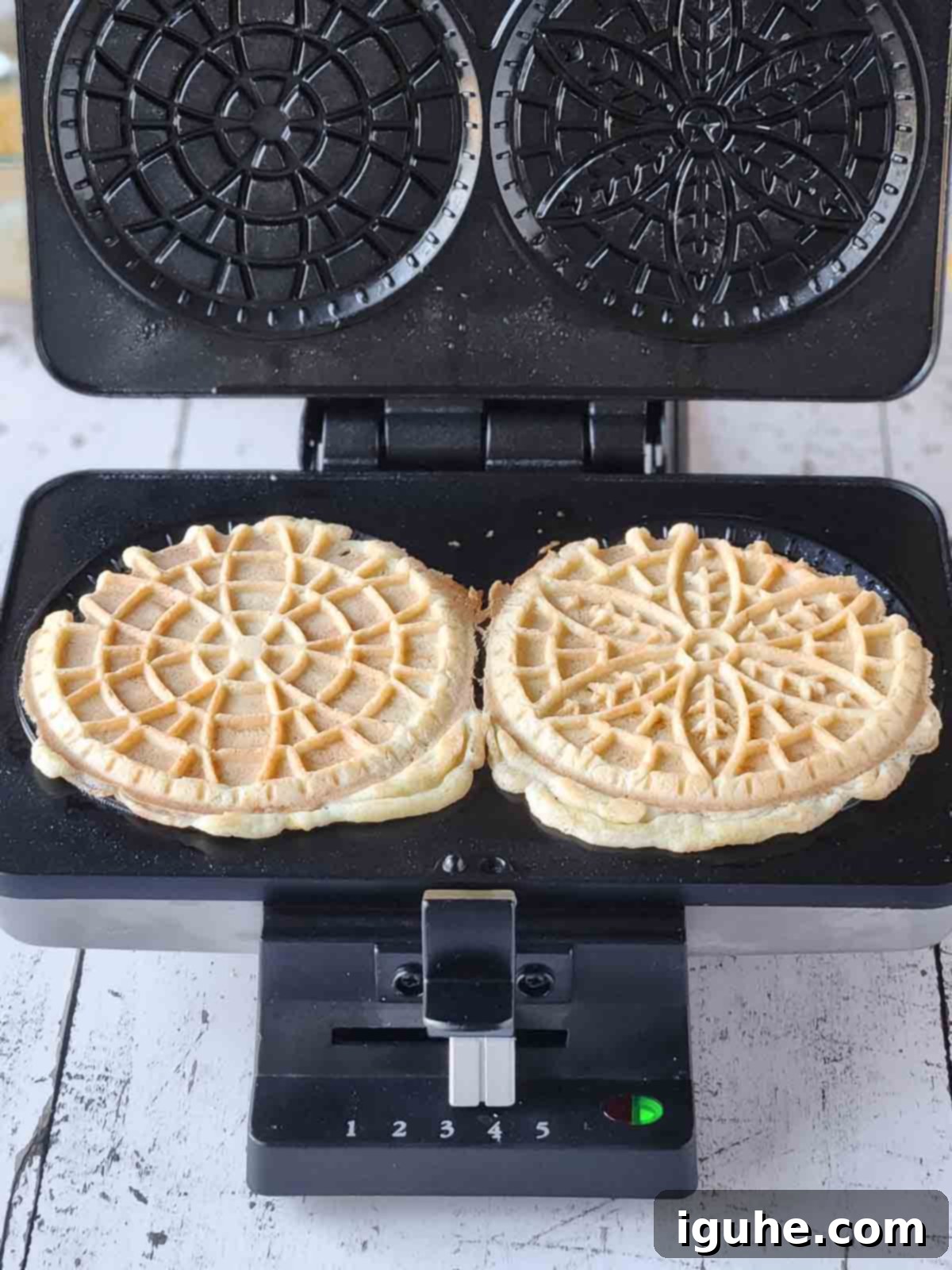 Effortless Lemon Pizzelle 10 Two cooked pizzelles in a pizzelle maker with the lid open, showing a slight overflow.