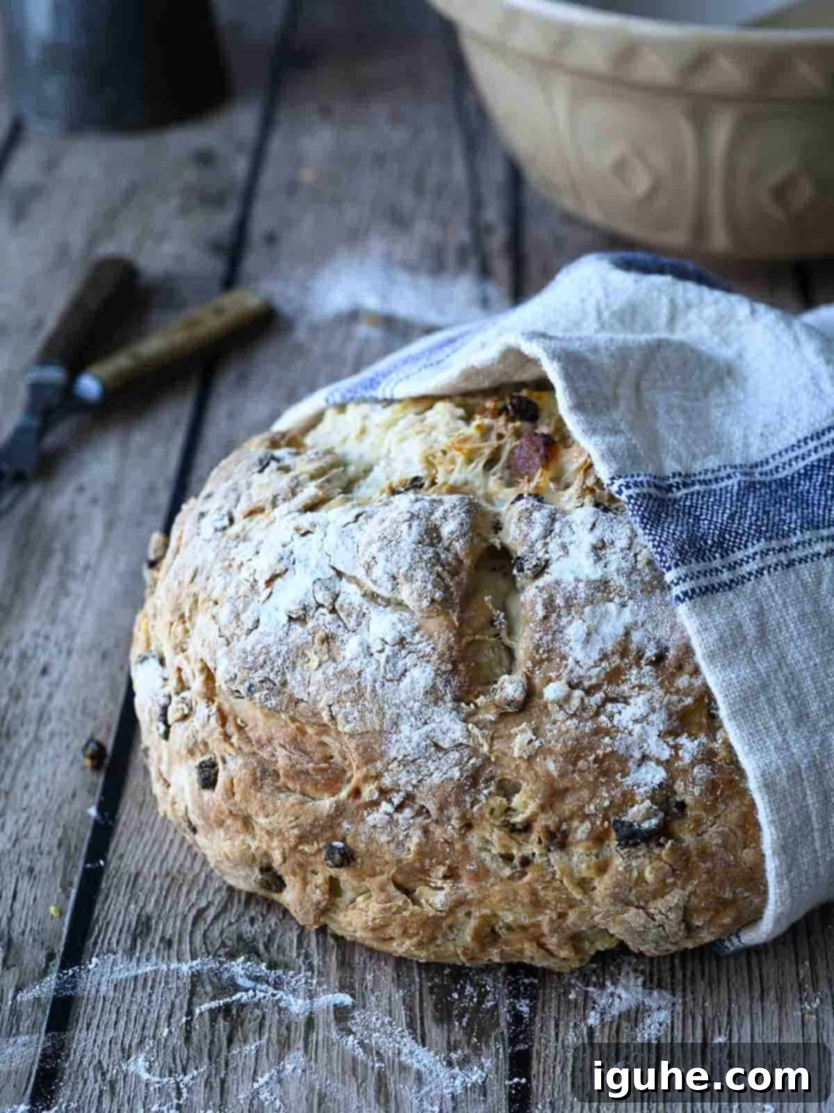 Sun-Kissed Apricot and Currant Irish Soda Bread 2 Irish soda bread loaf wrapped in a beige and blue towel on a wood surface.