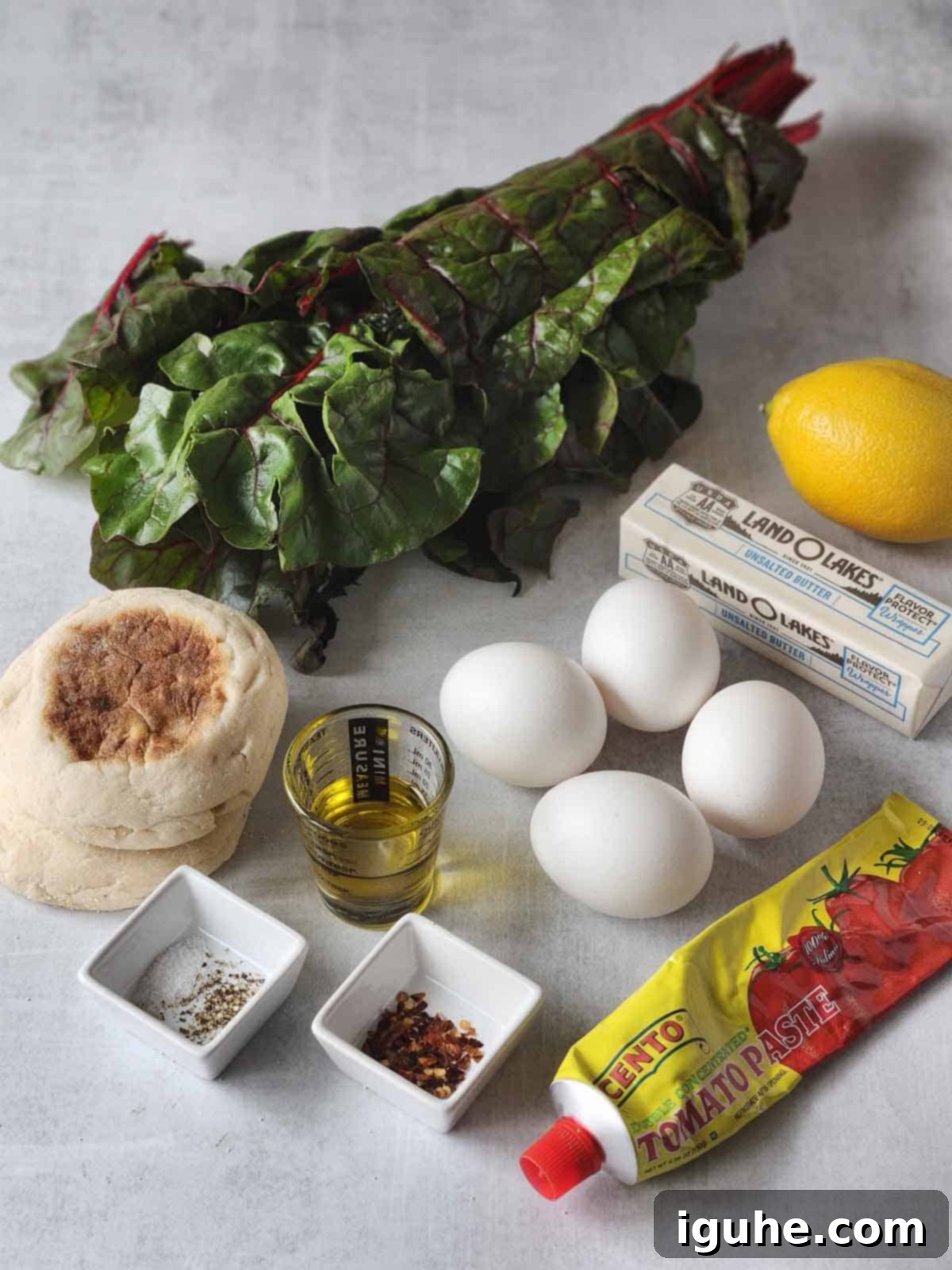 Swiss Chard Eggs Florentine with Zesty Tomato Hollandaise 3 Ingredients for Swiss chard eggs Florentine laid out on a grey surface, including fresh chard, eggs, lemon, and butter.