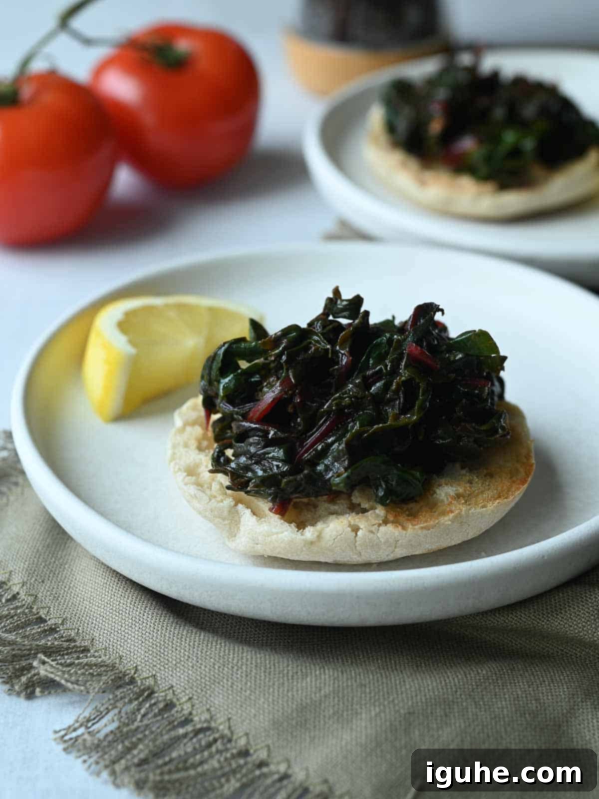Swiss Chard Eggs Florentine with Zesty Tomato Hollandaise 6 Two white plates with English muffins topped with cooked Swiss chard.