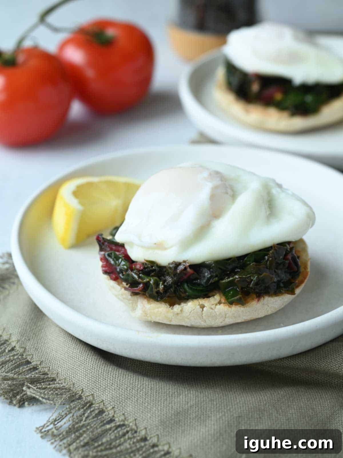 Swiss Chard Eggs Florentine with Zesty Tomato Hollandaise 7 Two white plates with English muffins, Swiss chard, and perfectly poached eggs.