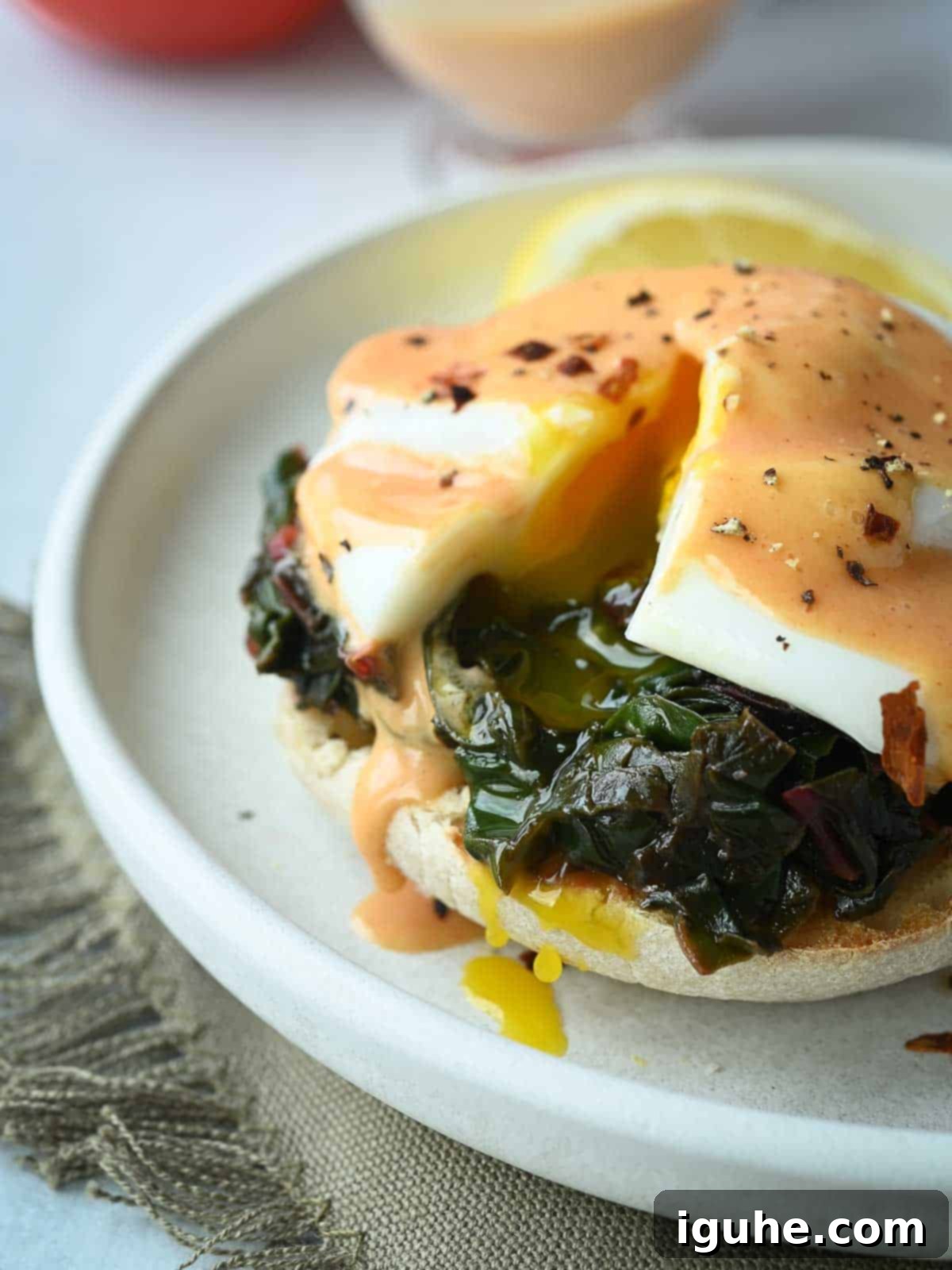 Swiss Chard Eggs Florentine with Zesty Tomato Hollandaise 9 Eggs Florentine with a poached egg cut open, revealing a runny yolk dripping onto a white plate, highlighting its deliciousness.