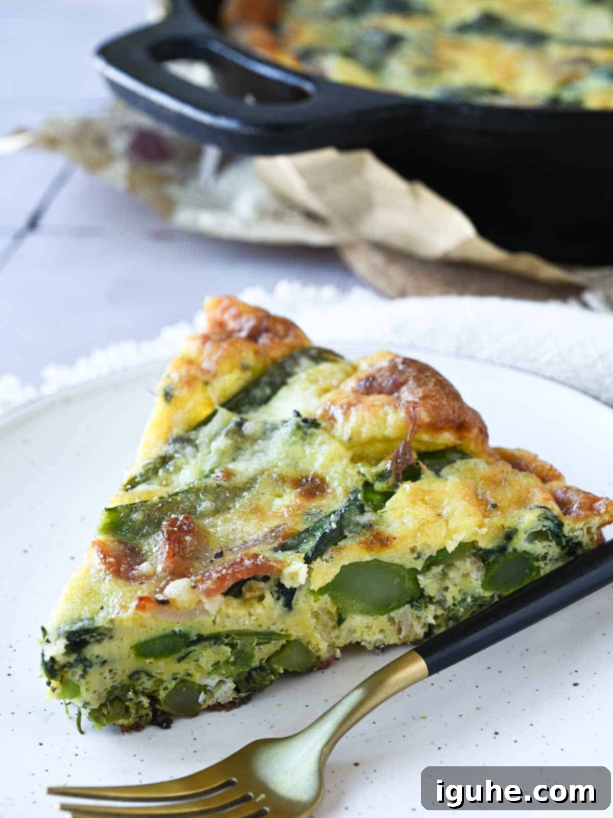 Ultimate Broccolini Bacon Parmesan Frittata 7 A slice of broccolini frittata on a beige plate with a fork next to it.