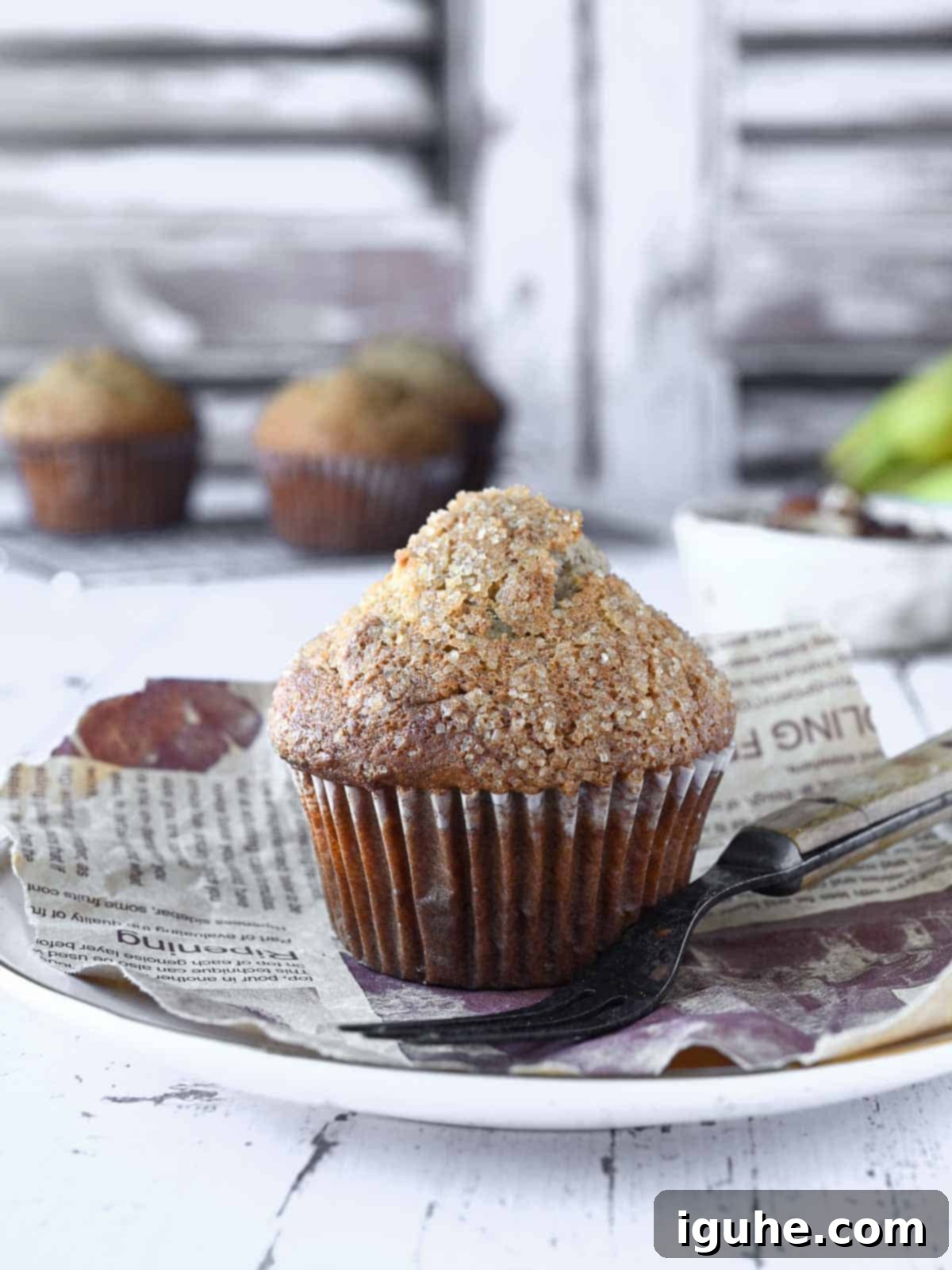 Irresistible Banana Pecan Muffins 10 Banana muffin on a white plate with muffins and pecans in the background.