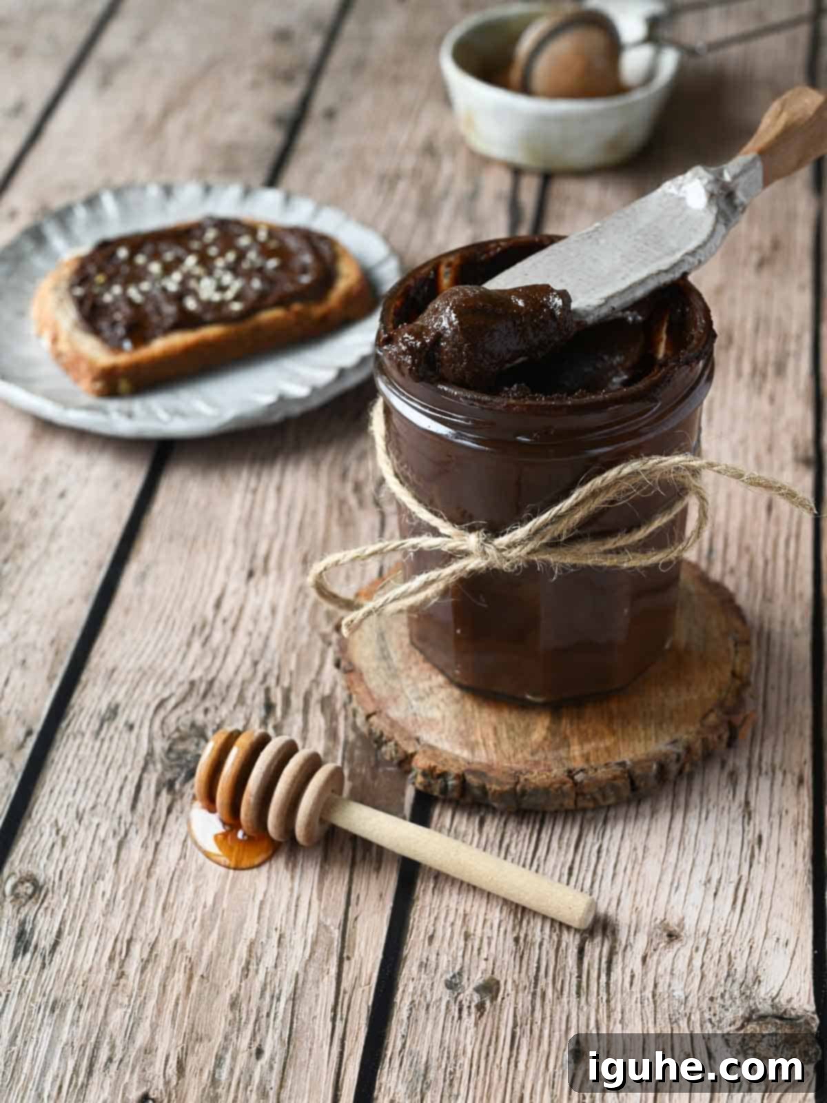Chocolate tahini spread in a clear jay with a spreader scooping some out.