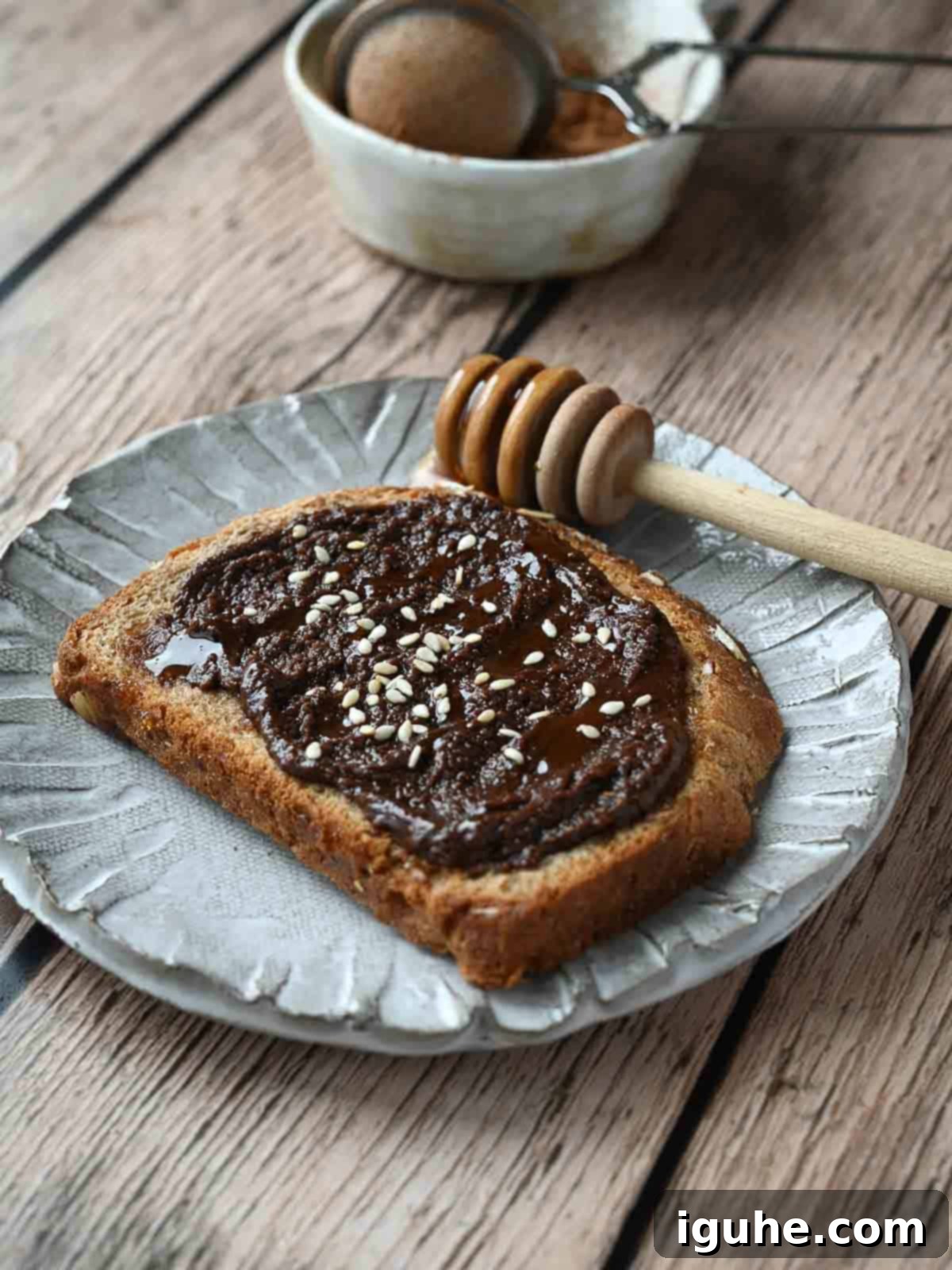 Chocolate tahini spread on toast with sesame seeds on top on top of a wood surface.