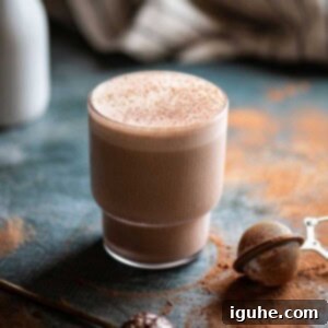 Decadent Chocolate Tahini Oat Milk Smoothie 8 A delectable Chocolate Tahini Oat Milk Smoothie in a clear glass on a blue surface, garnished with a sprinkle of cocoa powder.