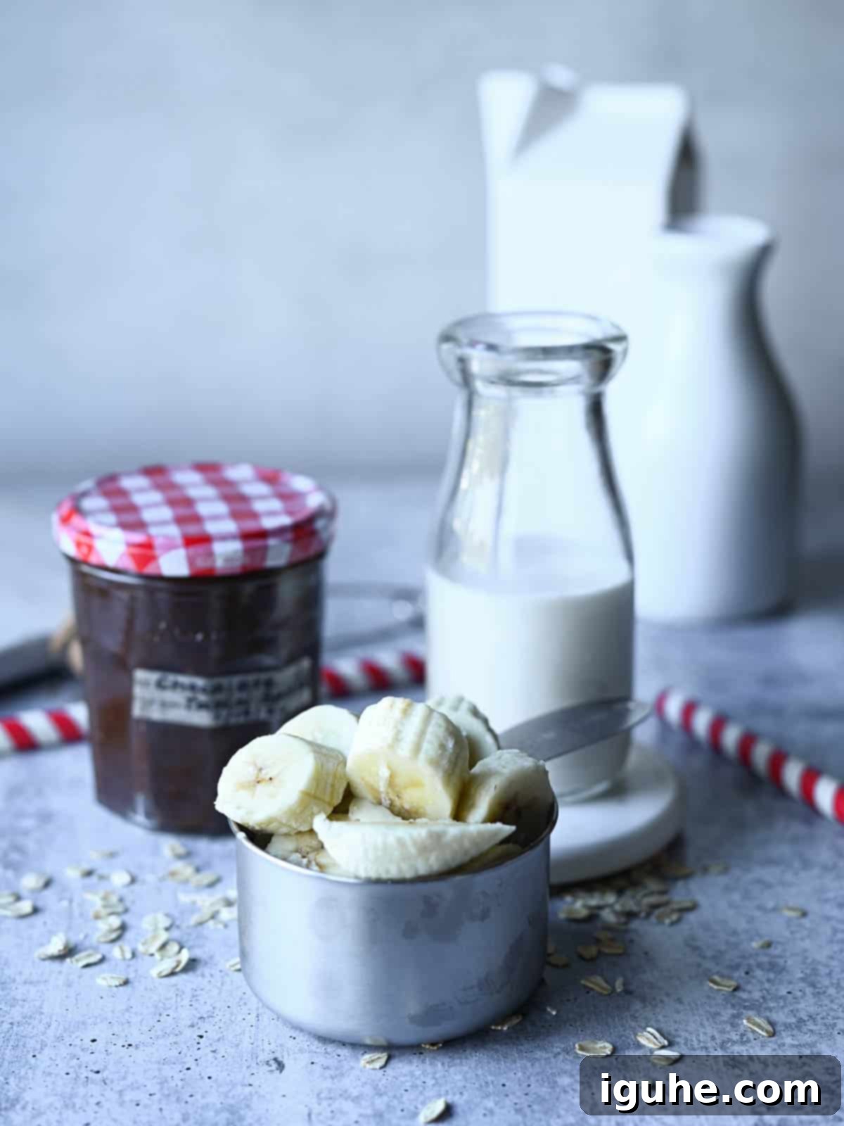 Decadent Chocolate Tahini Oat Milk Smoothie 3 Fresh ingredients laid out for a chocolate tahini smoothie on a grey background: frozen bananas, chocolate tahini, and oat milk.