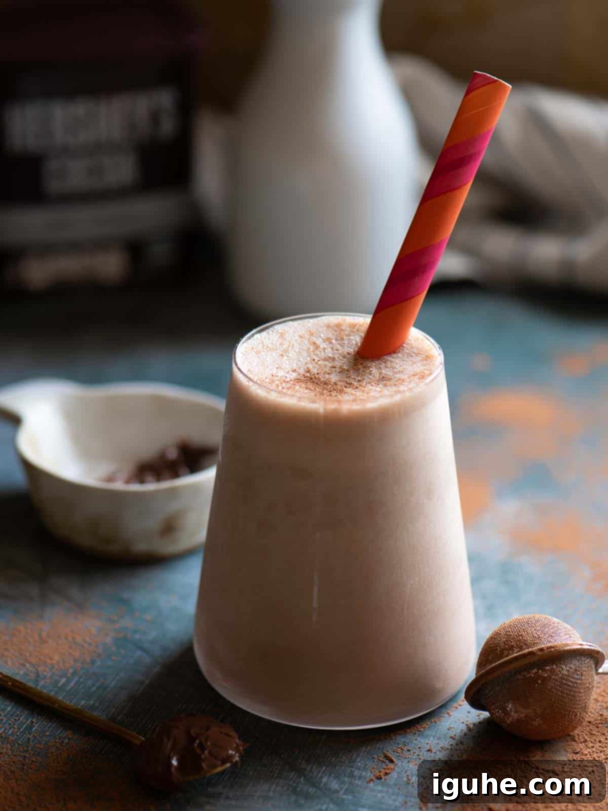 Decadent Chocolate Tahini Oat Milk Smoothie 6 Close-up of a rich chocolate tahini oat milk smoothie in a tall clear glass with an orange striped straw, ready to drink.