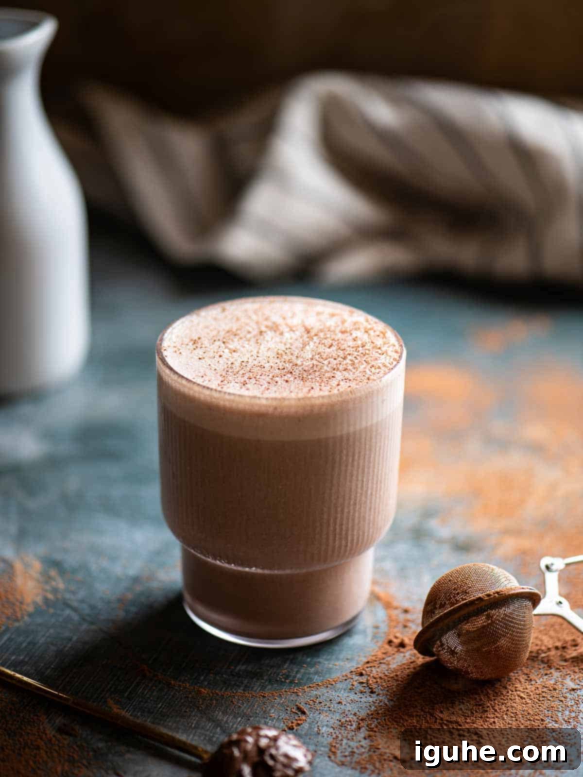 Decadent Chocolate Tahini Oat Milk Smoothie 7 Chocolate Tahini Oat Milk Smoothie in a clear glass, lightly dusted with cocoa powder for garnish, on a rustic surface.