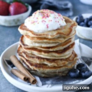 Cinnamon Swirl Sweet Cream Pancakes 10 A generous stack of fluffy cinnamon sweet cream pancakes, artfully topped with whipped cream and colorful sprinkles, set against a muted grey background.