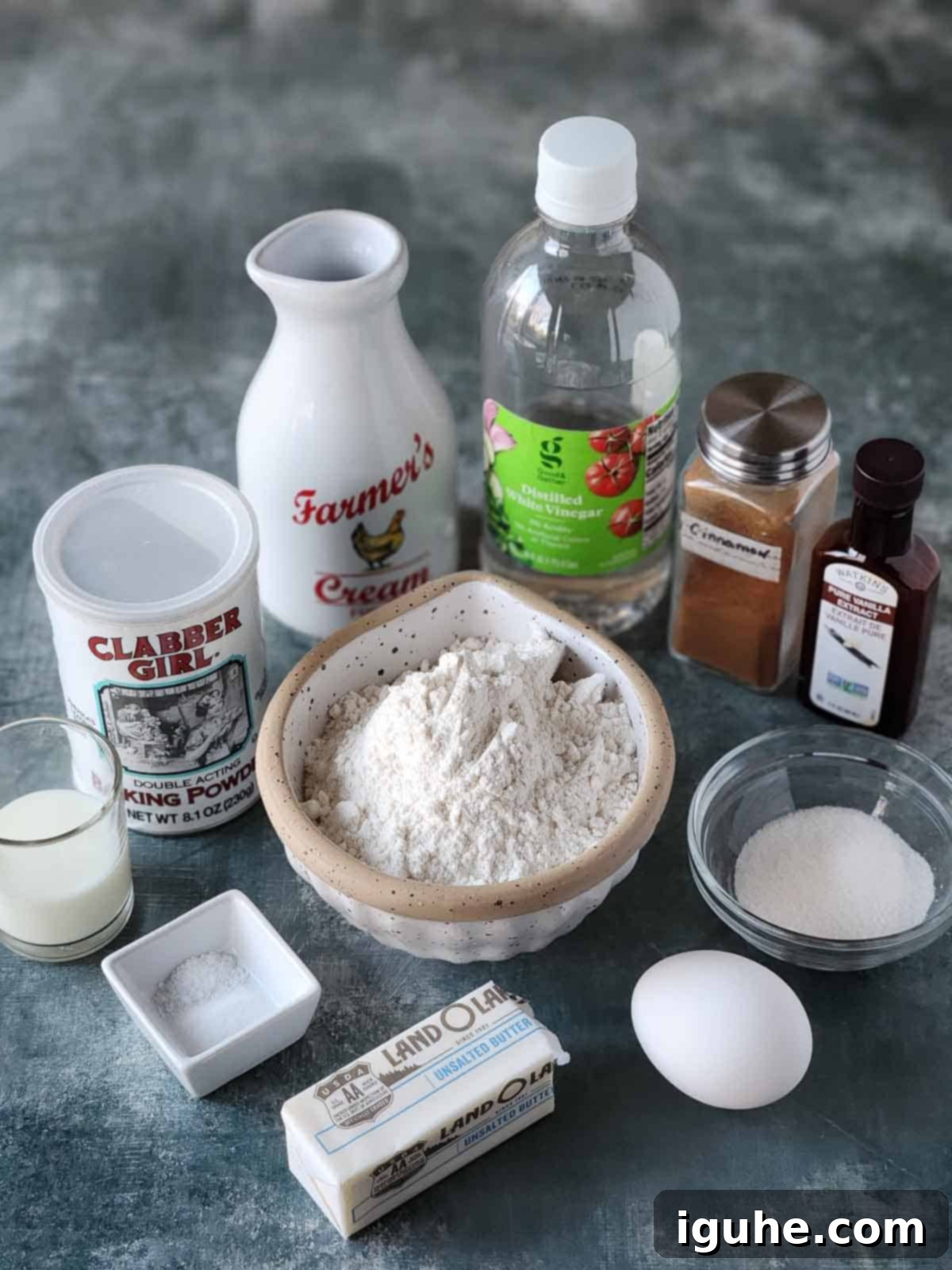 Cinnamon Swirl Sweet Cream Pancakes 3 A selection of raw ingredients for sweet cream pancakes laid out on a grey surface, including flour, heavy cream, eggs, butter, sugar, and spices.