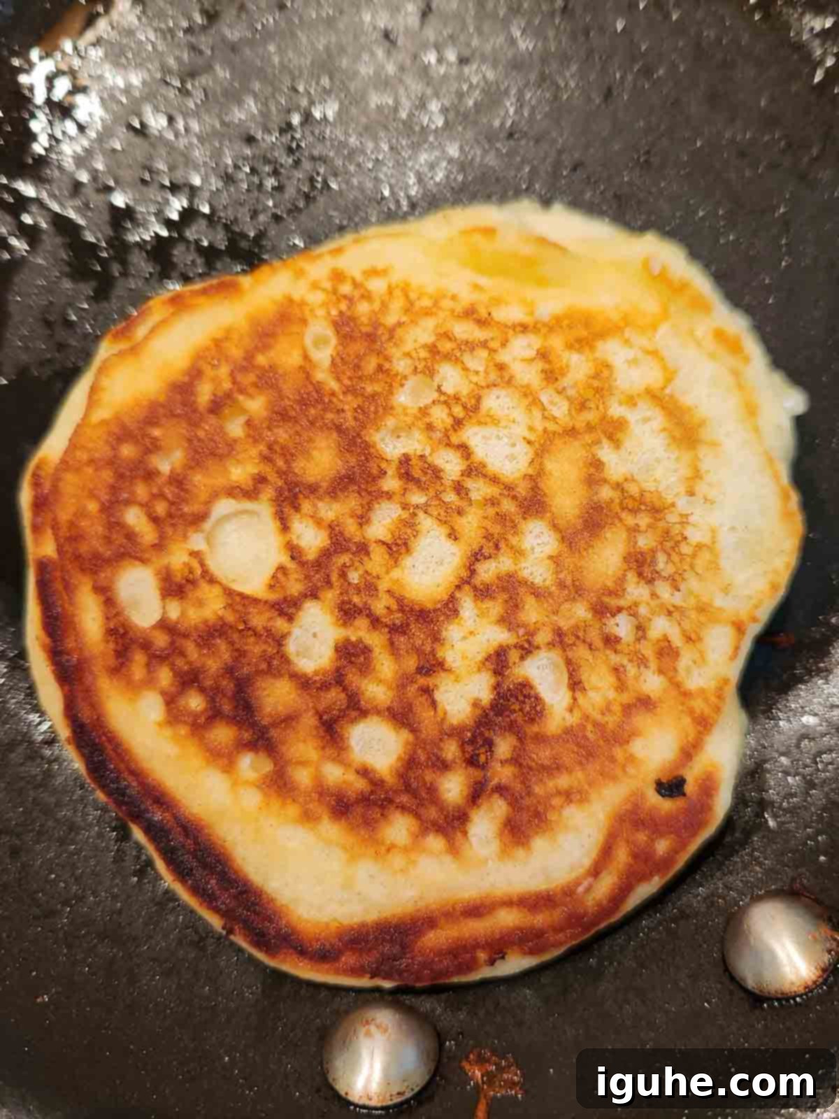 Cinnamon Swirl Sweet Cream Pancakes 7 A sweet cream pancake just flipped in a skillet, revealing a golden-brown underside with crispy edges.