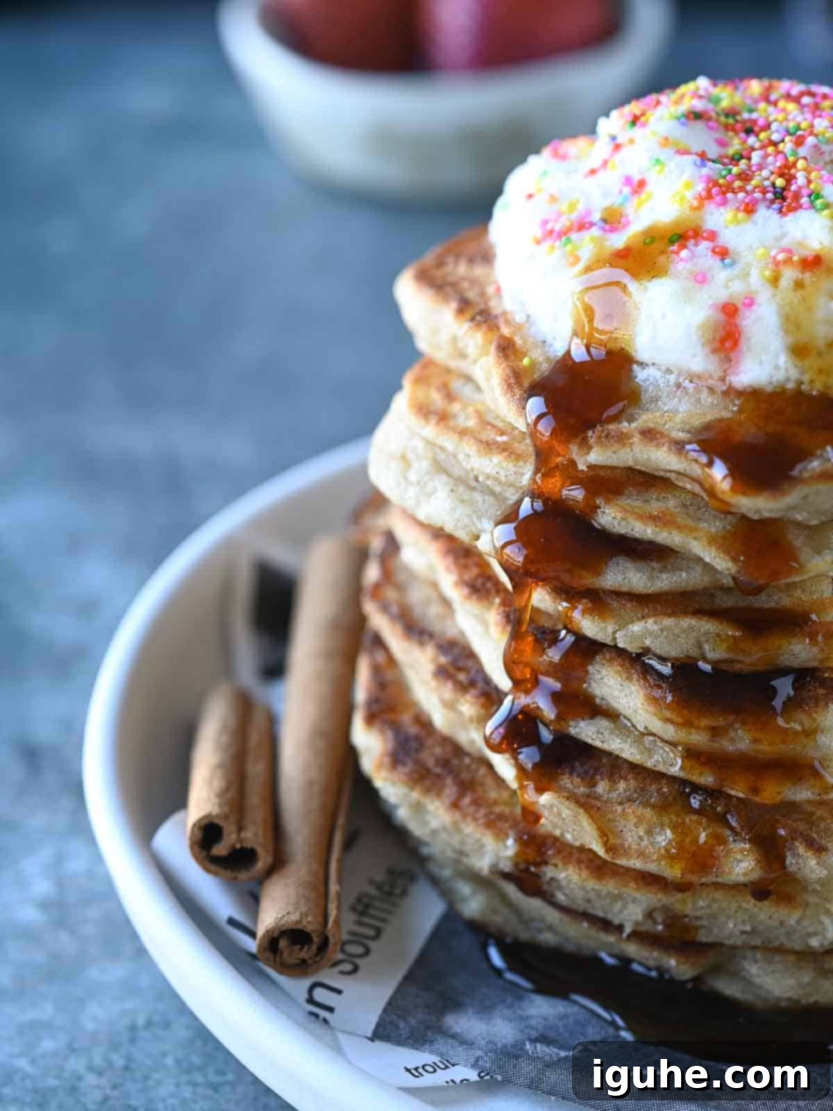 Cinnamon Swirl Sweet Cream Pancakes 8 Close-up of a stack of sweet cream pancakes adorned with whipped cream and rich maple syrup cascading down the sides, presented on a grey surface.