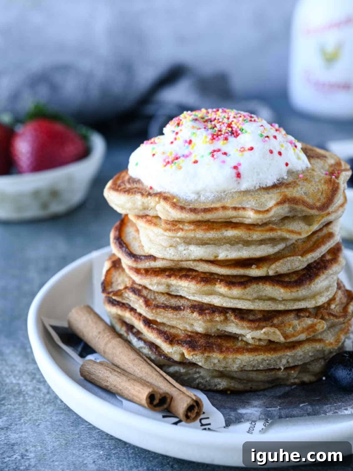 Cinnamon Swirl Sweet Cream Pancakes 9 A perfectly stacked tower of sweet cream pancakes, generously topped with whipped cream and colorful sprinkles, on a simple grey background.