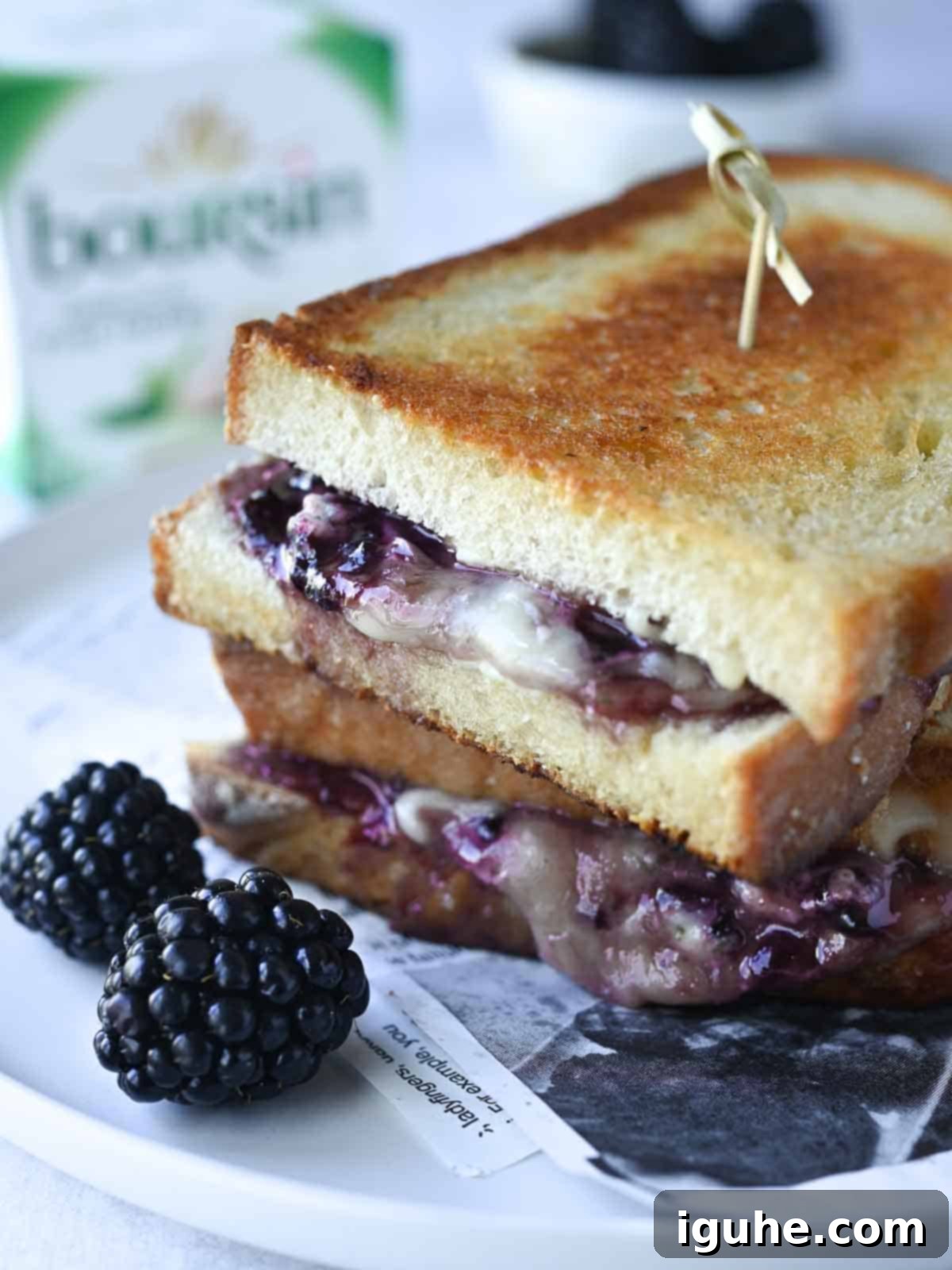 Blackberry Boursin grilled cheese on a white plate with fresh blackberries in the foreground, showcasing a perfect golden crust and creamy filling.