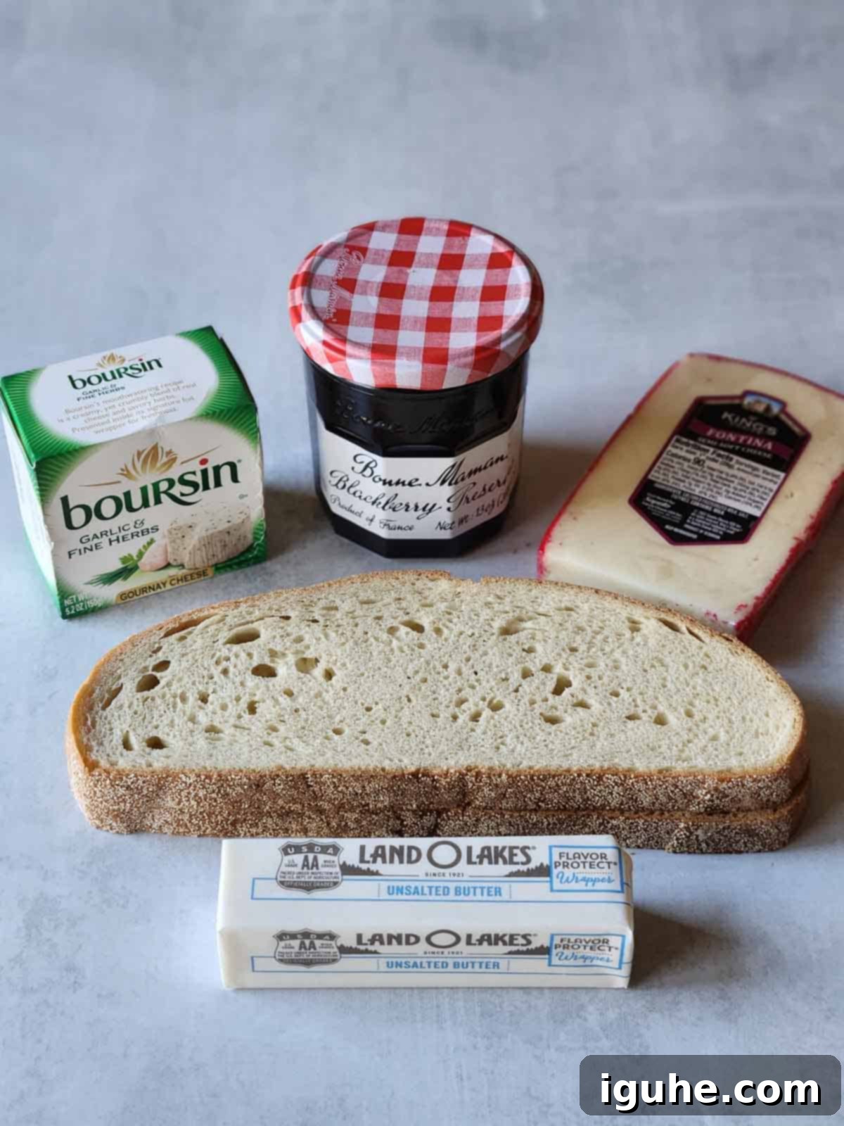 Blackberry Boursin Grilled Delight 3 Ingredients for blackberry Boursin grilled cheese laid out on a grey surface, including bread, jam, Boursin, Fontina, and butter.