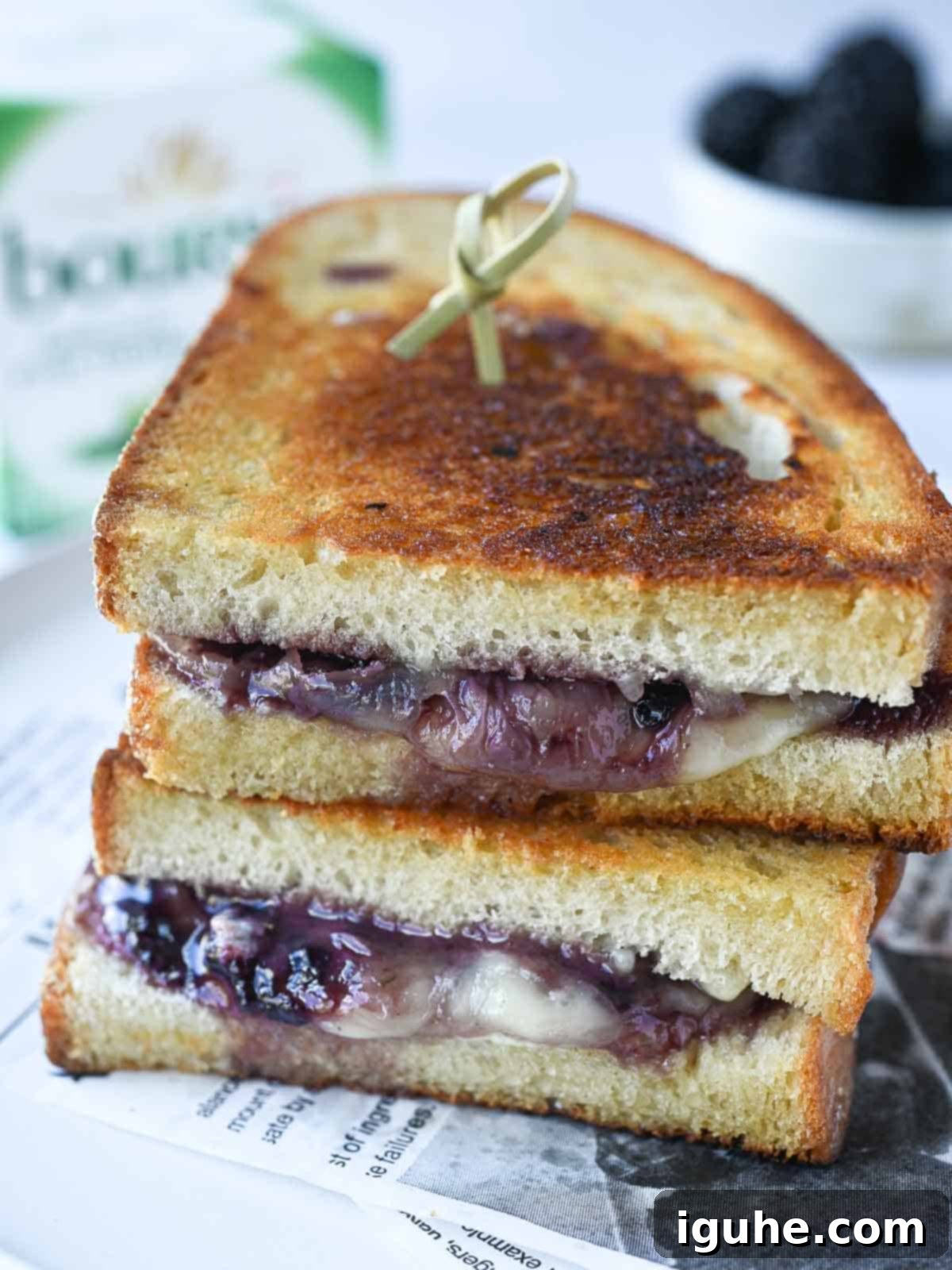 Blackberry Boursin Grilled Delight 6 Two stacked Blackberry Boursin grilled cheese sandwiches on a white plate with a block of Boursin cheese in the background.