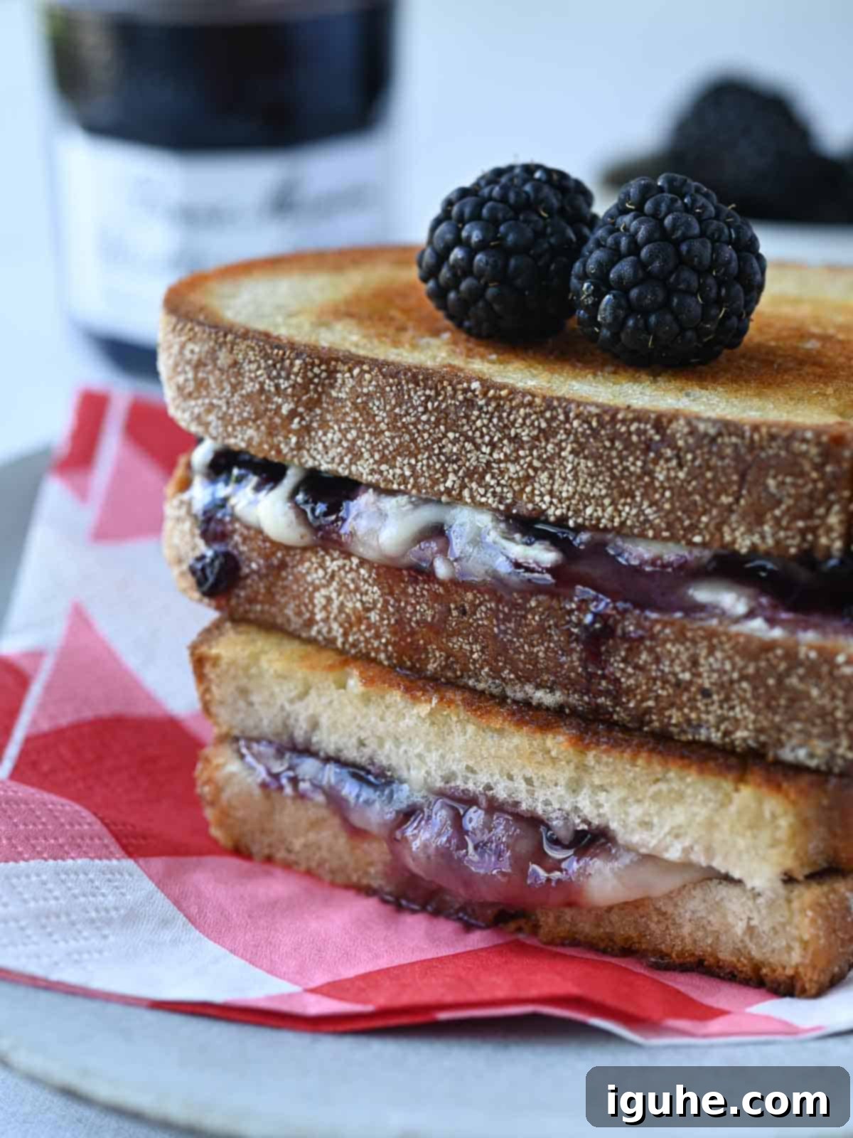 Blackberry Boursin Grilled Delight 7 Blackberry Boursin grilled cheese stacked on a white plate with a red checkered napkin underneath, ready to be enjoyed.