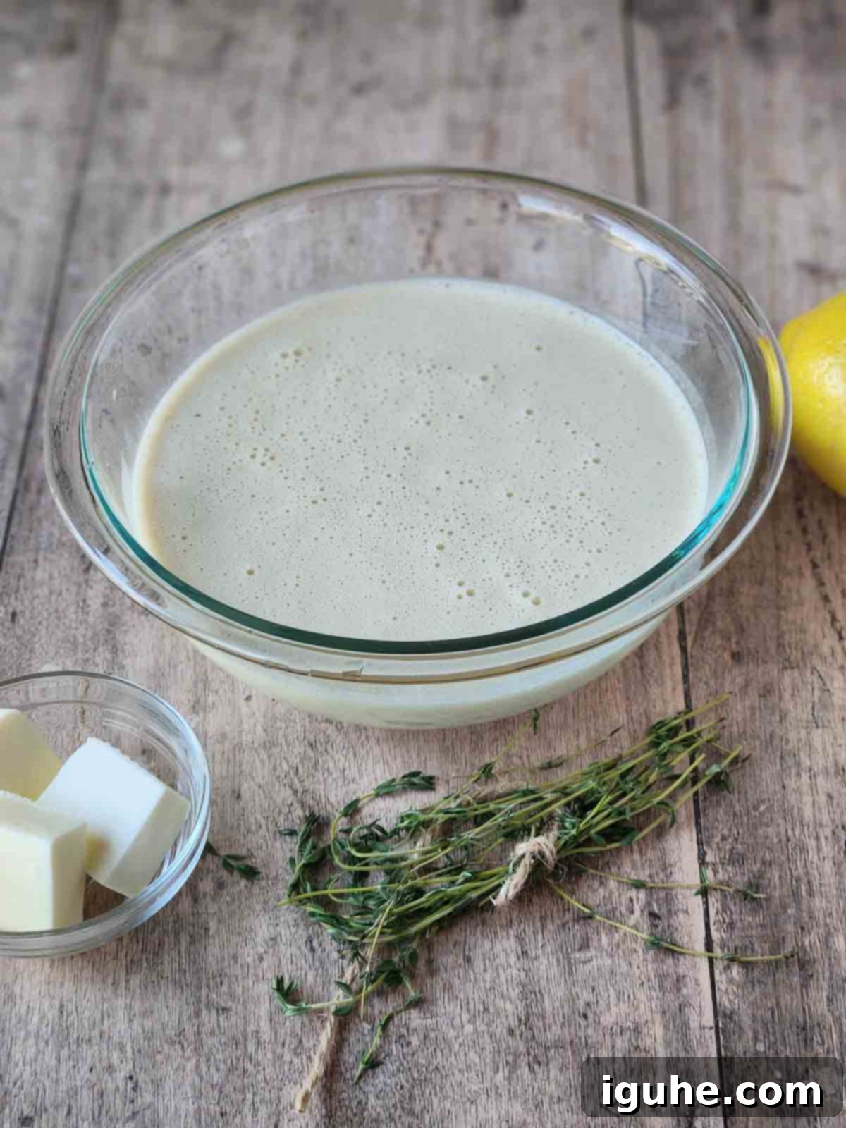 Fluffy Lemon Thyme Delights 4 Smooth, pale yellow batter for lemon thyme popovers resting in a clear glass bowl on a rustic wood surface.