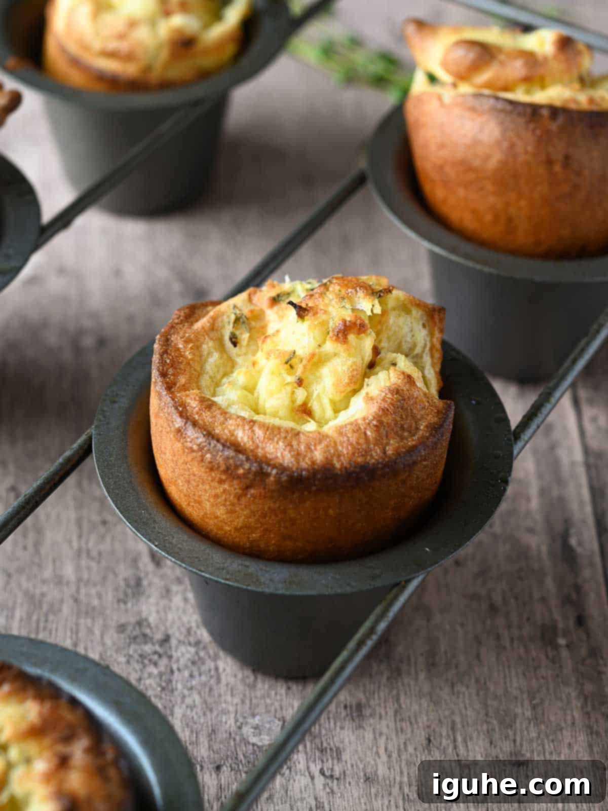 Fluffy Lemon Thyme Delights 8 Freshly baked lemon and thyme popovers perfectly puffed up in a specialized popover pan on a rustic wooden surface.