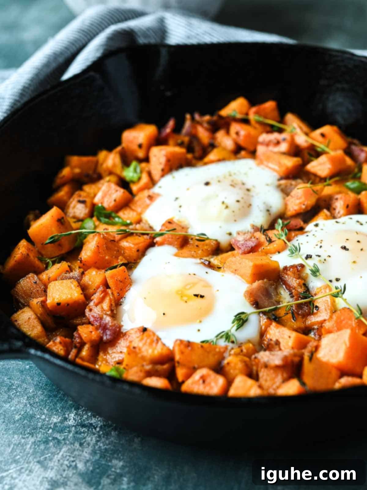 Sunrise Sweet Potato Bacon Medley 2 Sweet potato hash in a cast iron skillet with 3 fried eggs in it.