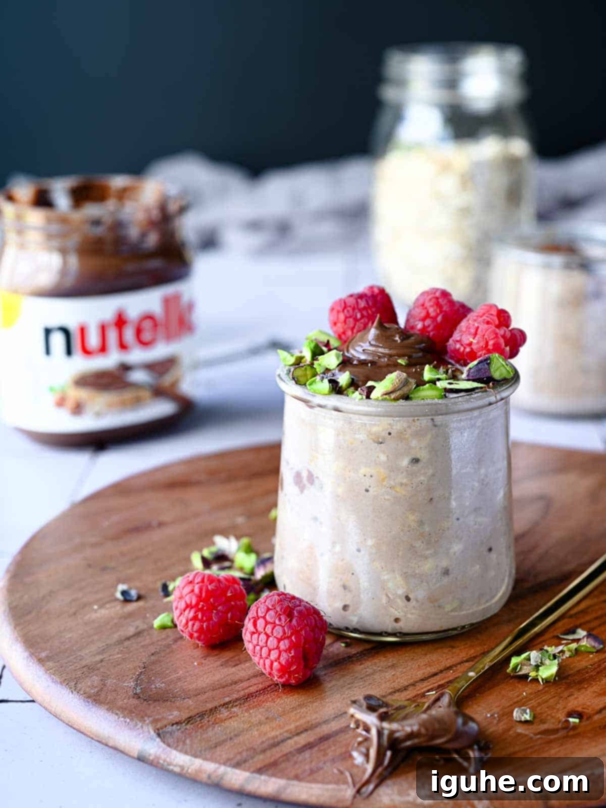 Nutella overnight oats in a clear jar with raspberries and pistachios on wood.