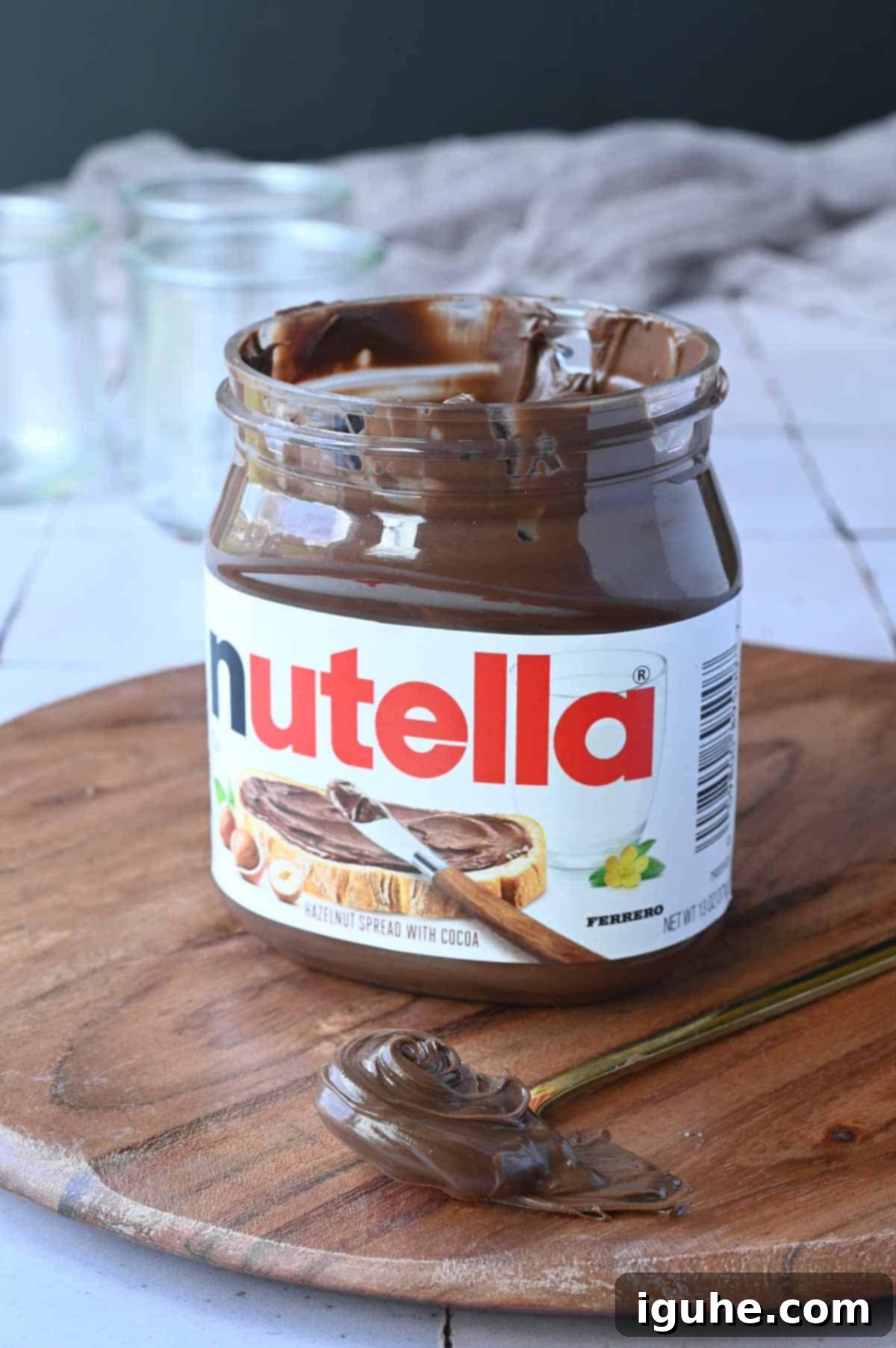 Decadent Nutella Overnight Oats 3 Jar of Nutella on a wood board with a spoon of Nutella next to it.