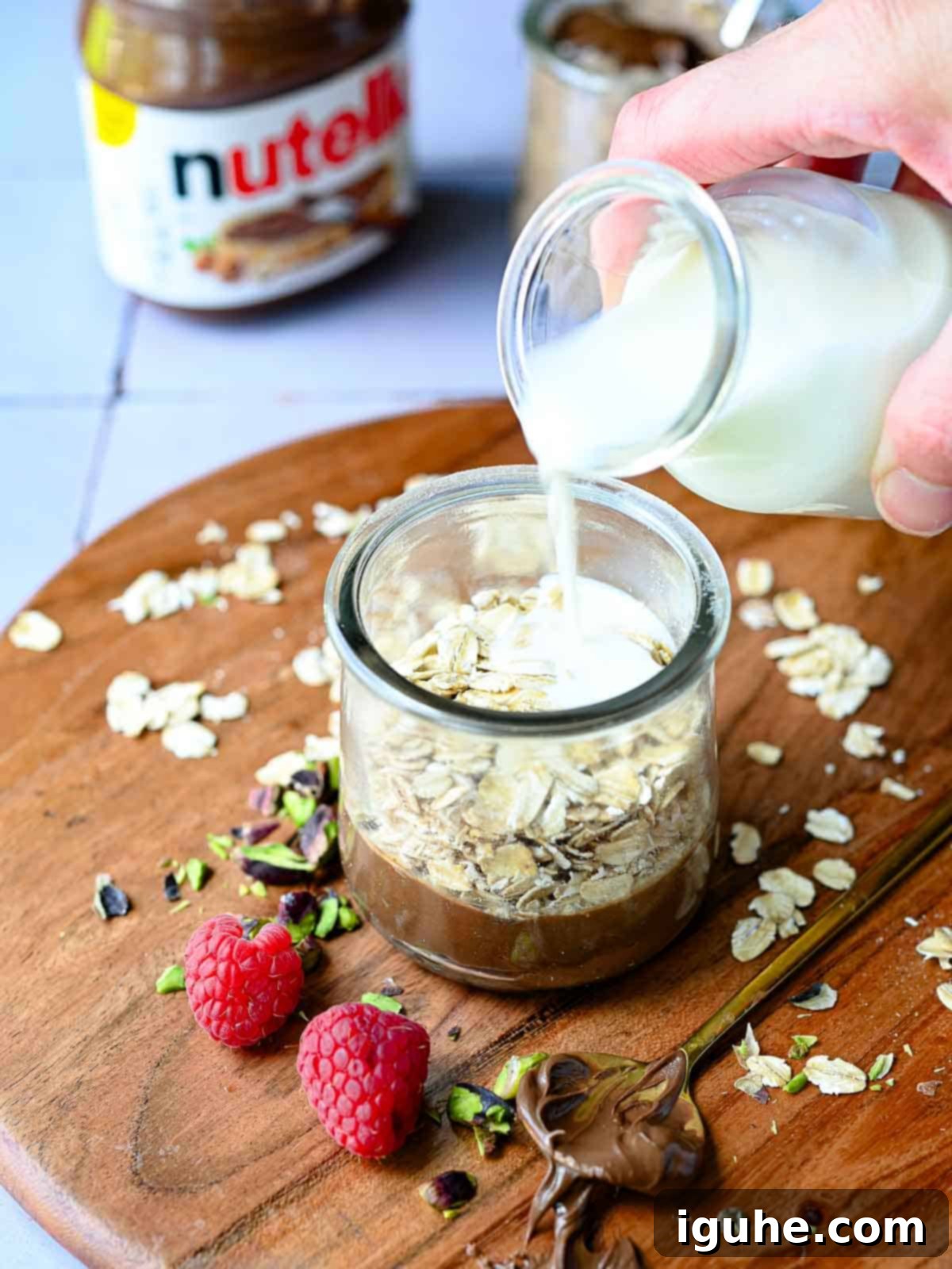 Decadent Nutella Overnight Oats 4 Milk is poured into a jar of oats and Nutella on wood.