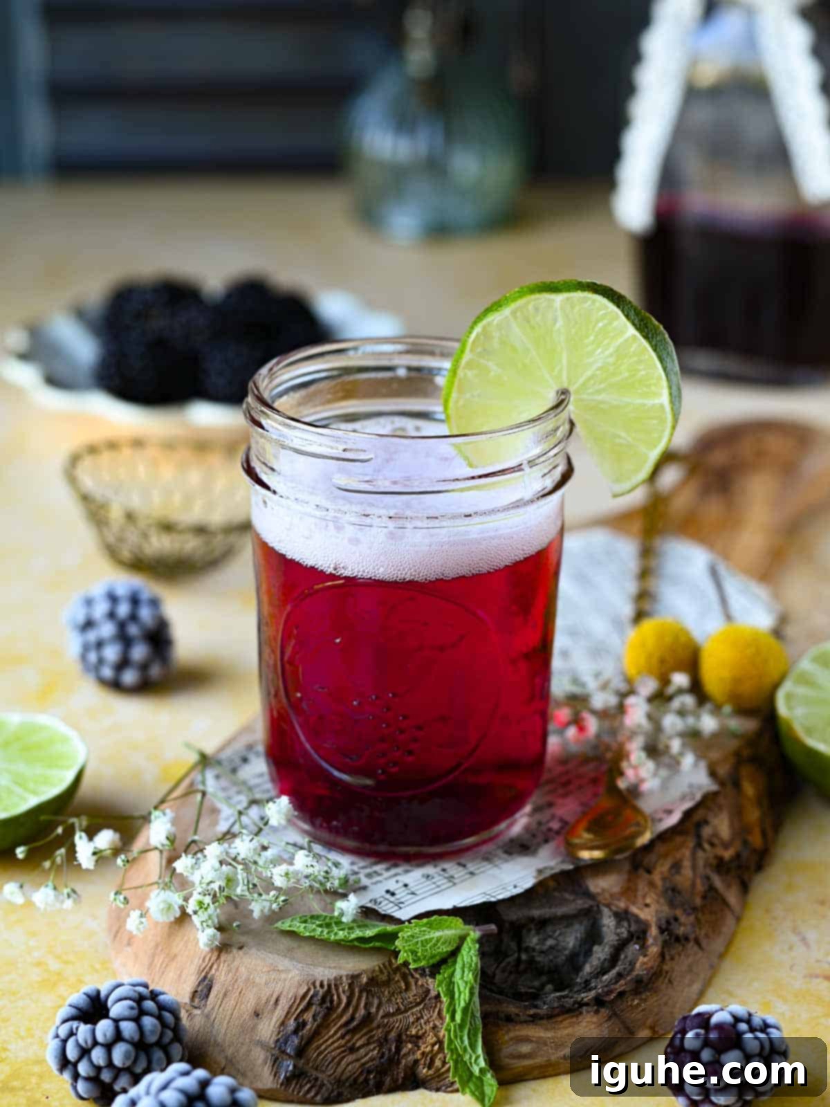 Blackberry Sparkler 4 Blackberry soda in a clear glass with a lime wedge on a yellow surface.